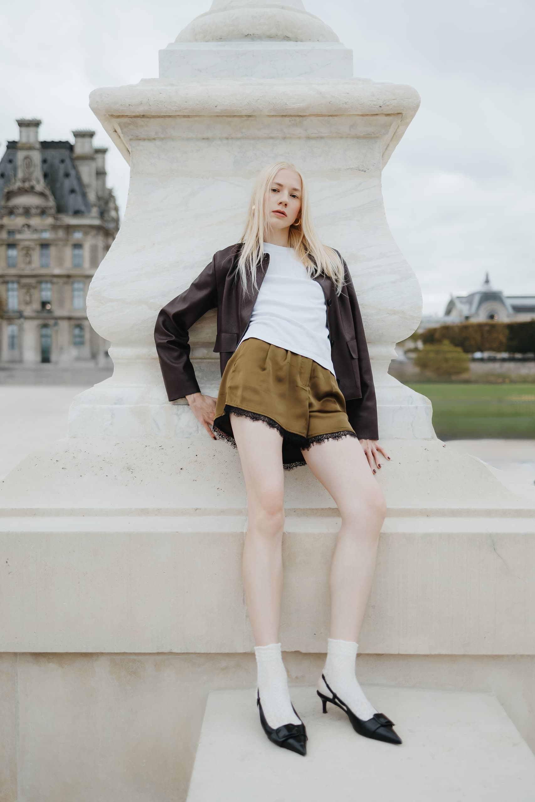 Fashionable woman leaning on stone structure, wearing stylish outfit and heels.