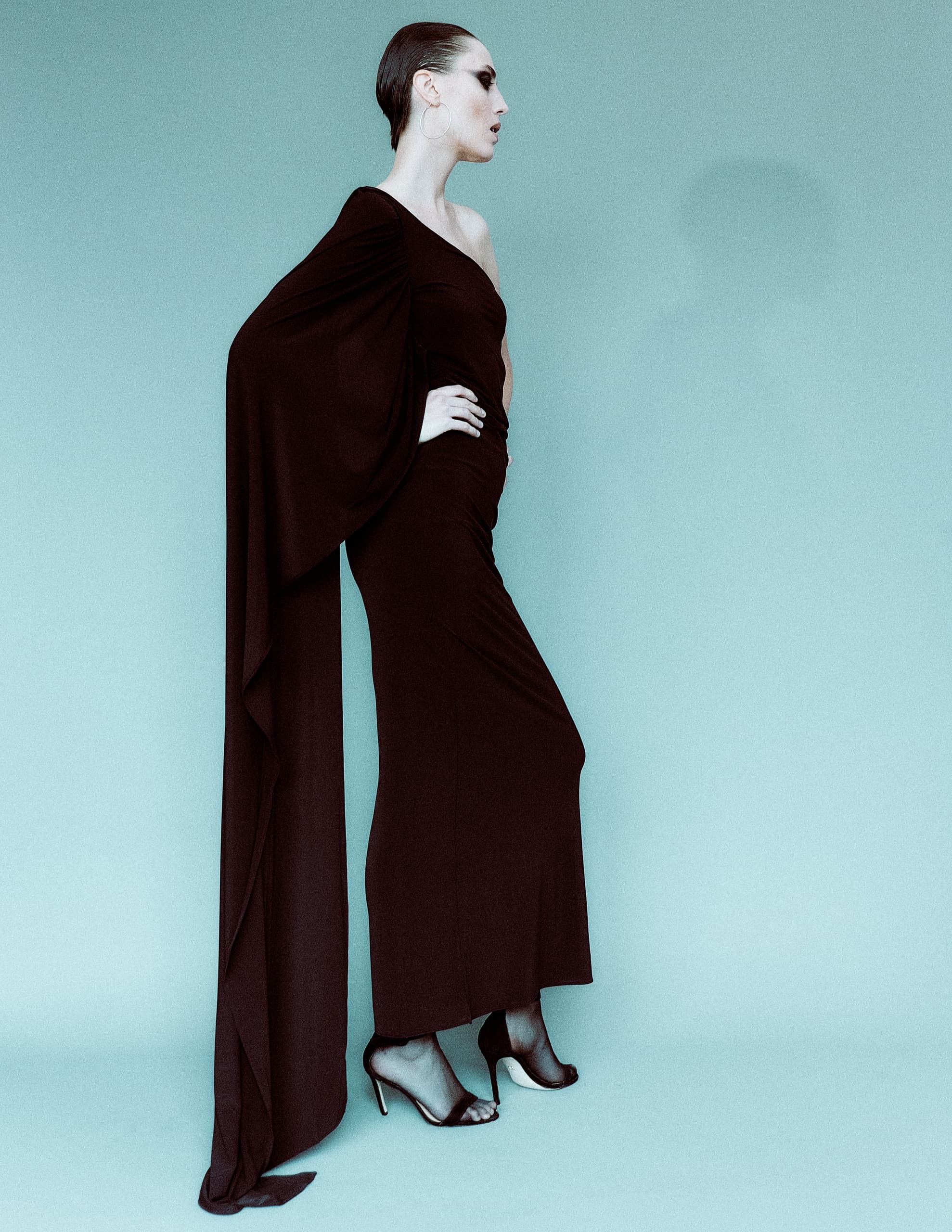 Fashion model in elegant black gown against blue background.