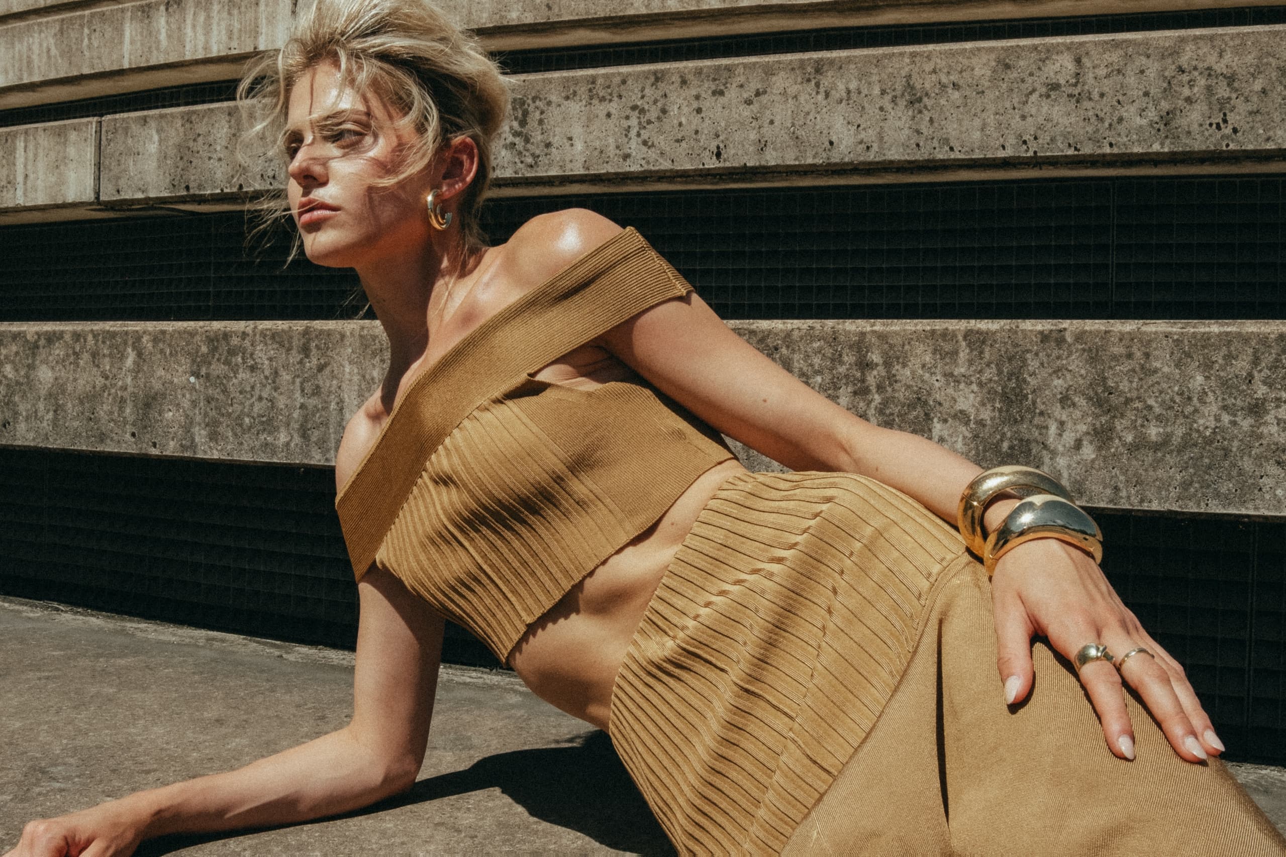 Woman in stylish tan outfit relaxing on sunlit concrete steps.