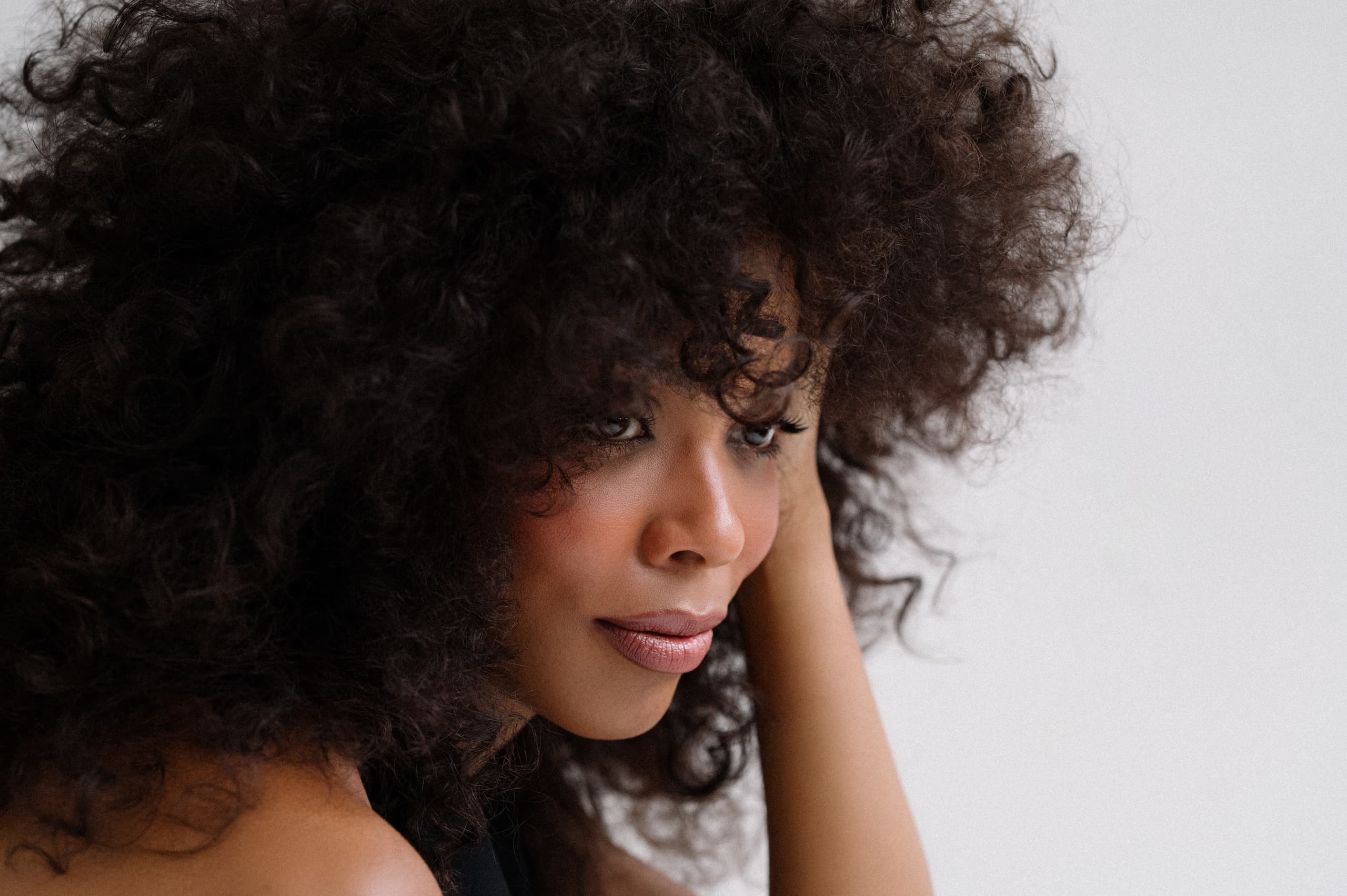 Woman with curly hair looks thoughtfully to the side.