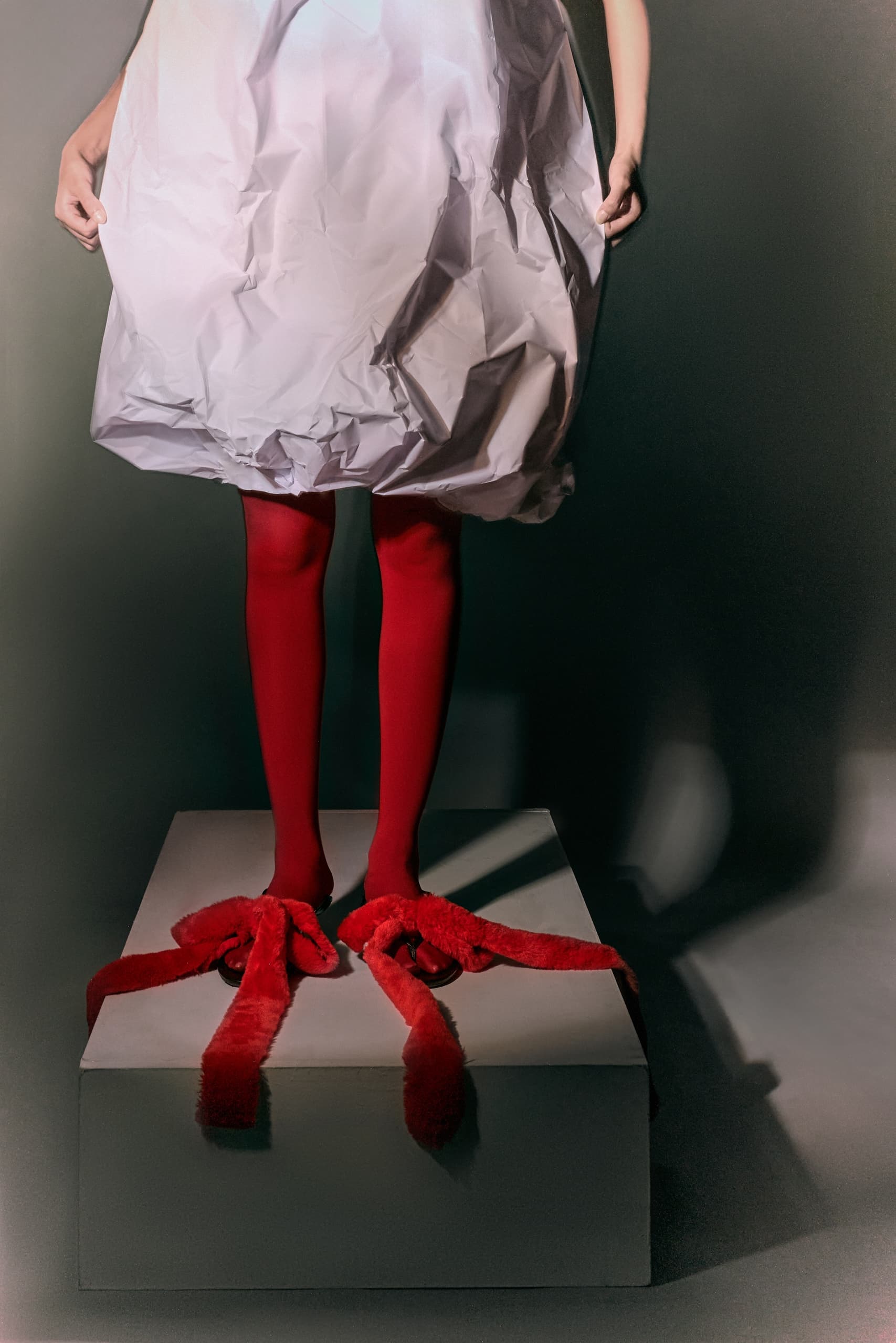 Person in red stockings and oversized shoes on a pedestal, wearing a crinkled dress.