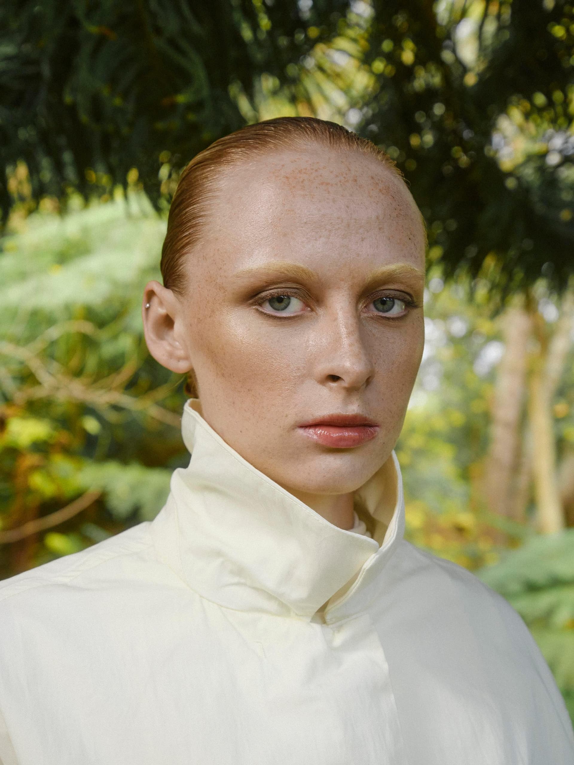 Close-up of a person in a white coat surrounded by lush greenery outdoors.