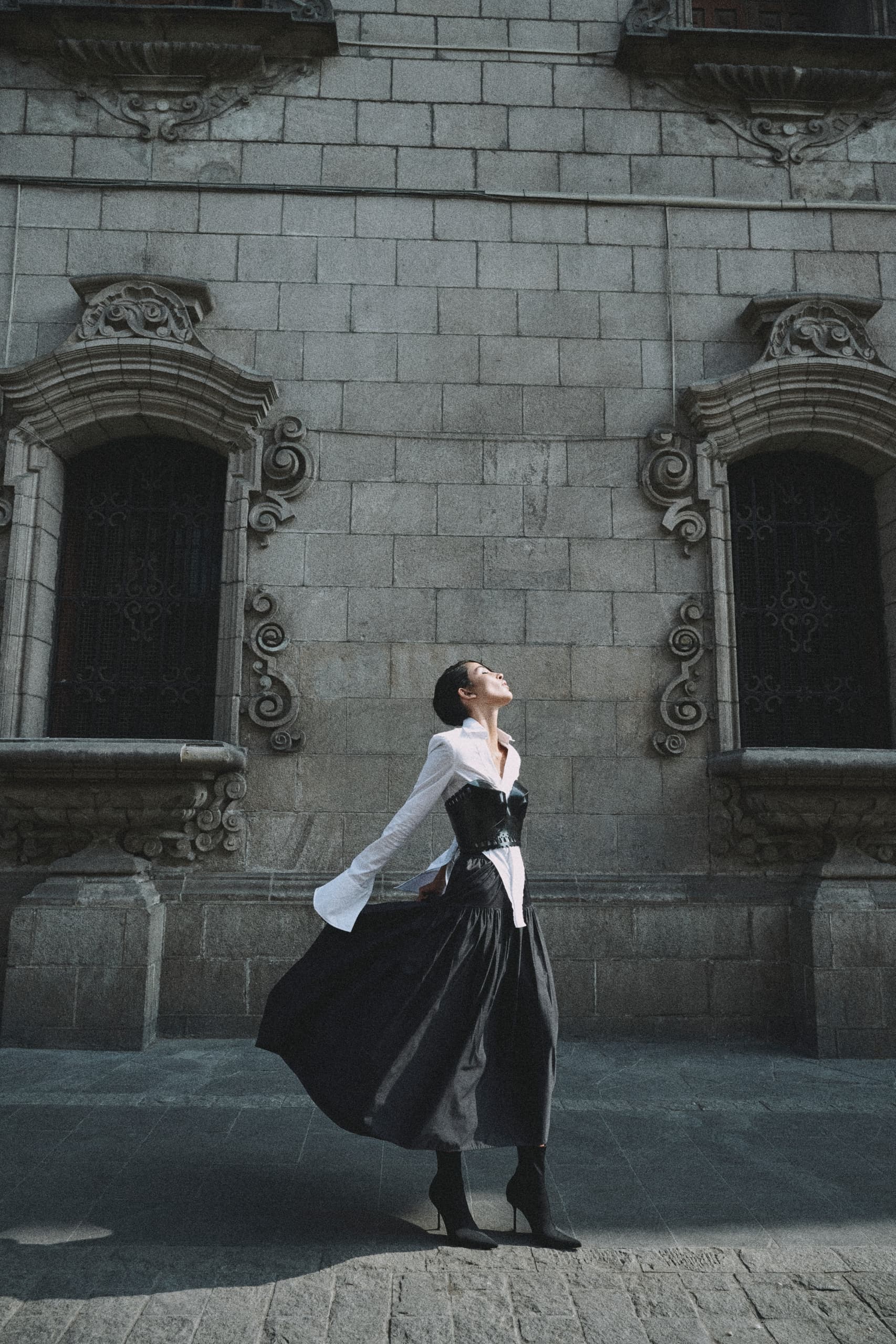 Fashionable woman in black dress posing against ornate stone building background.