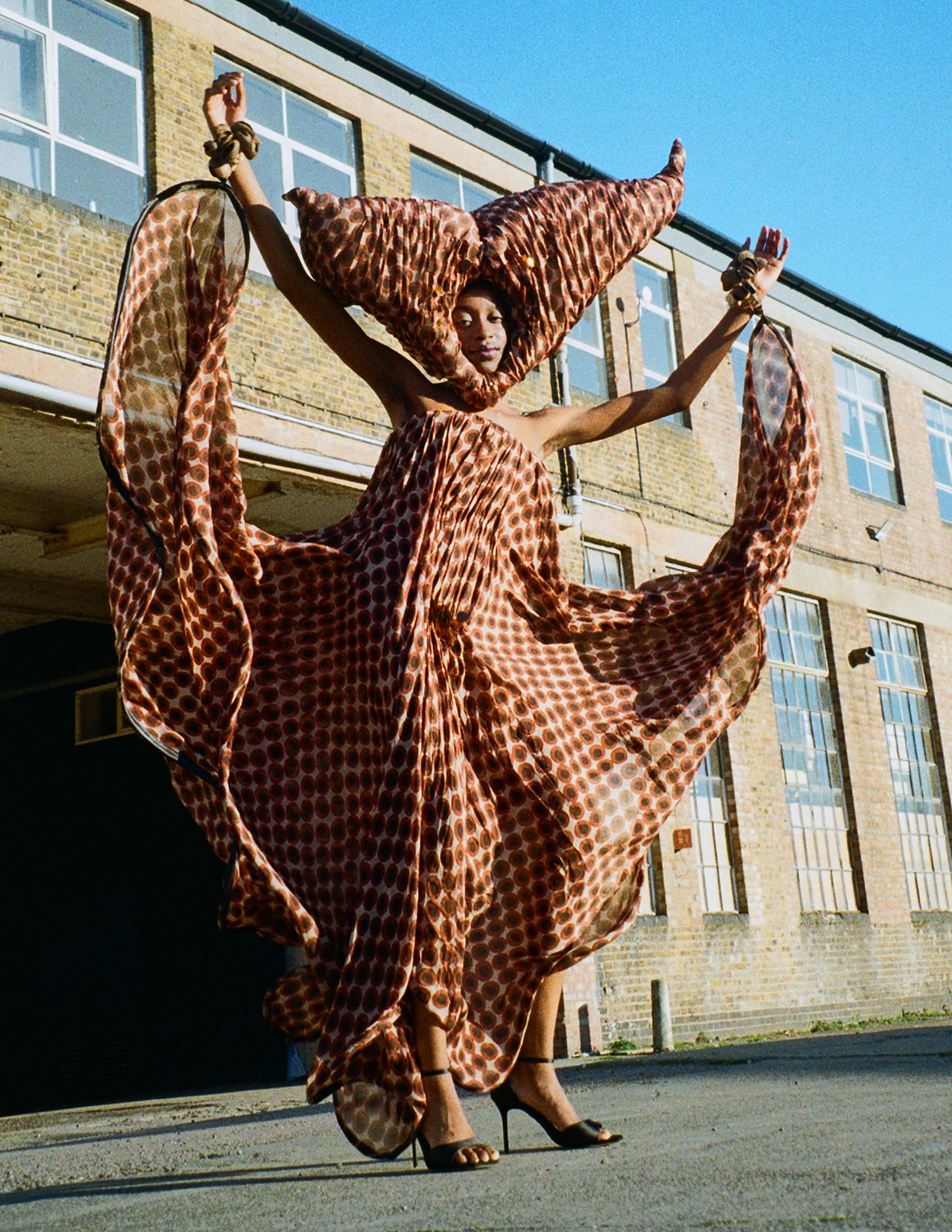 Person in a flowing, geometric-patterned dress with architectural backdrop.