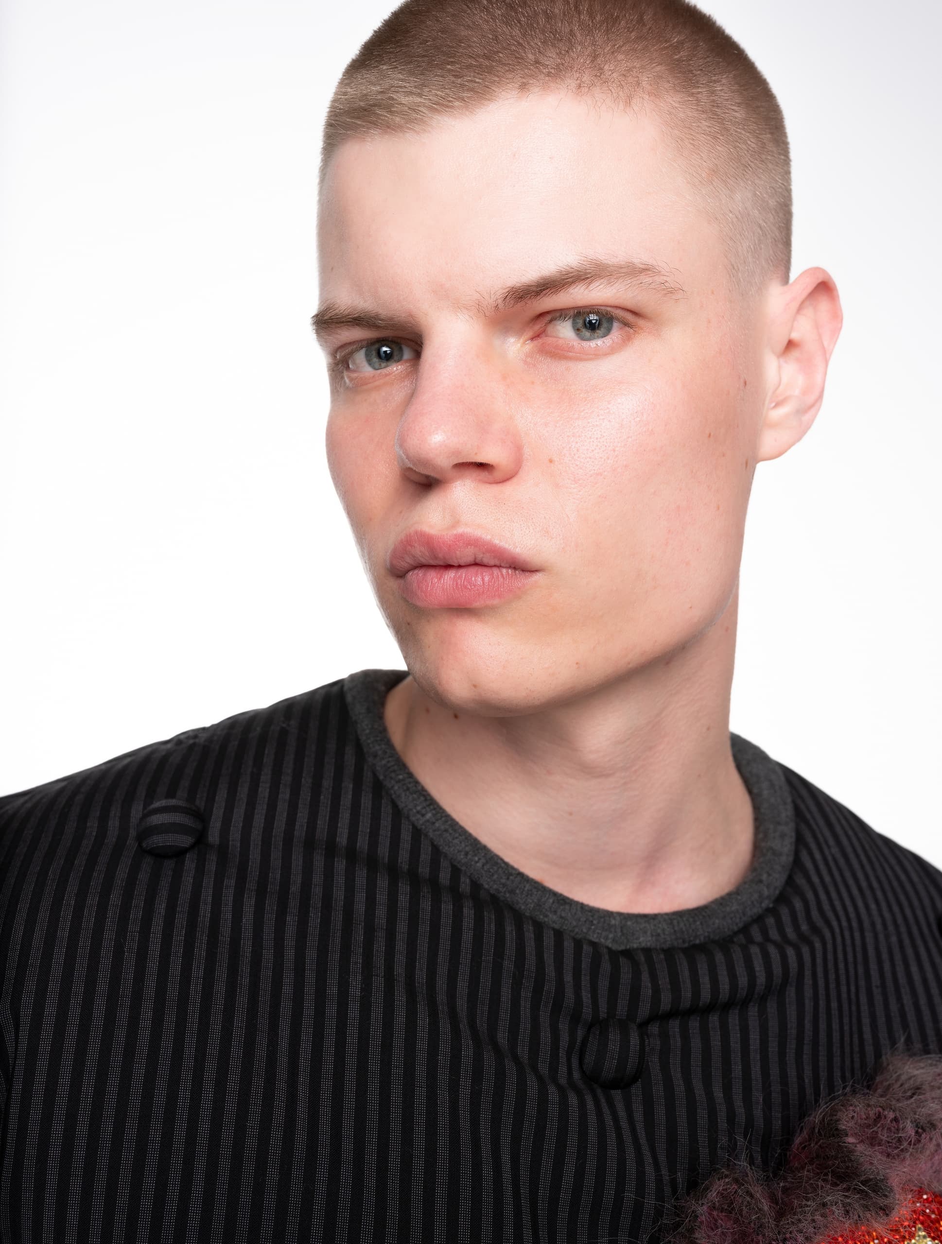 Young man with buzz cut in black striped shirt on a white background.