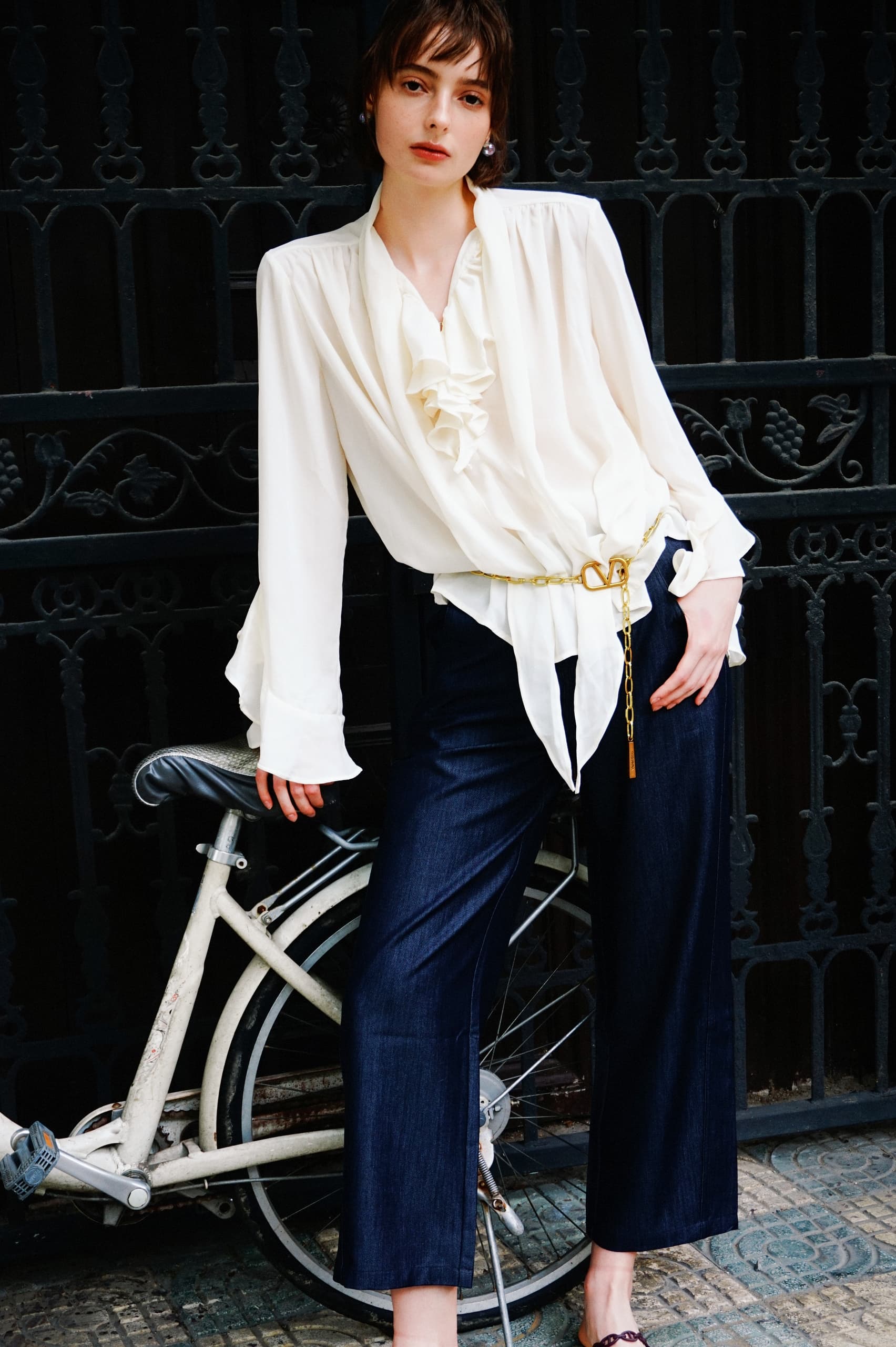 Fashionable woman in white blouse and navy pants leaning on a bicycle.