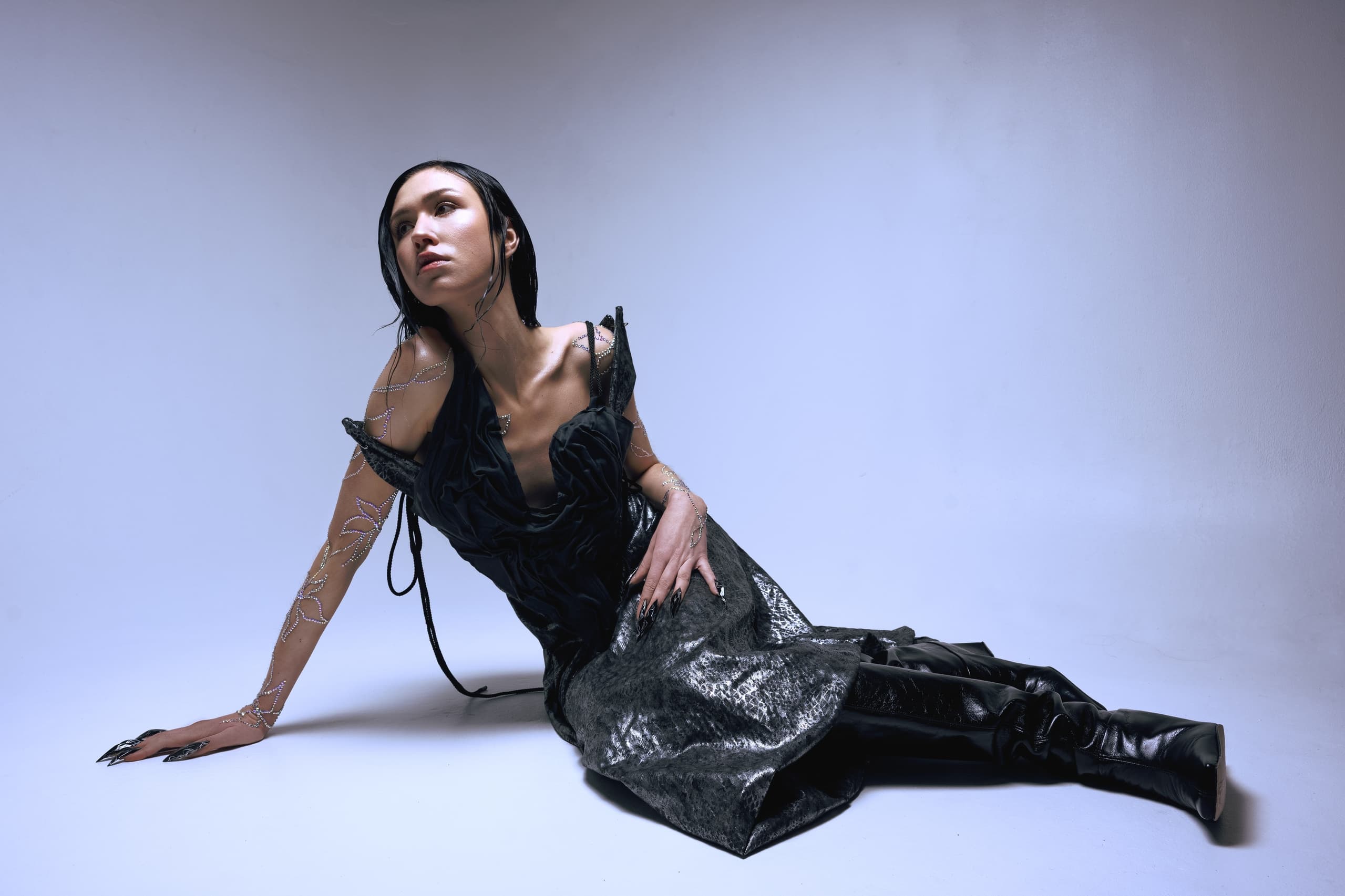 Woman in avant-garde black dress poses on floor, dramatic lighting.