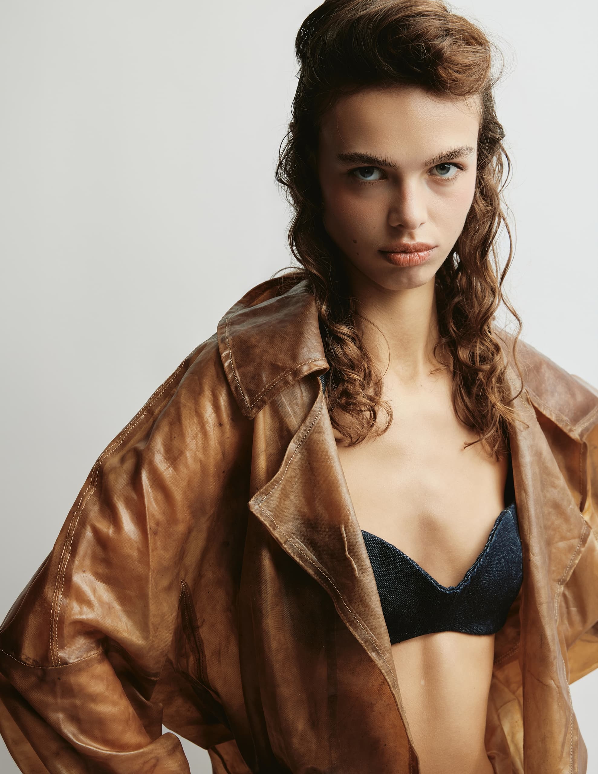 Person in a stylish brown jacket and denim top, photographed against a light background.