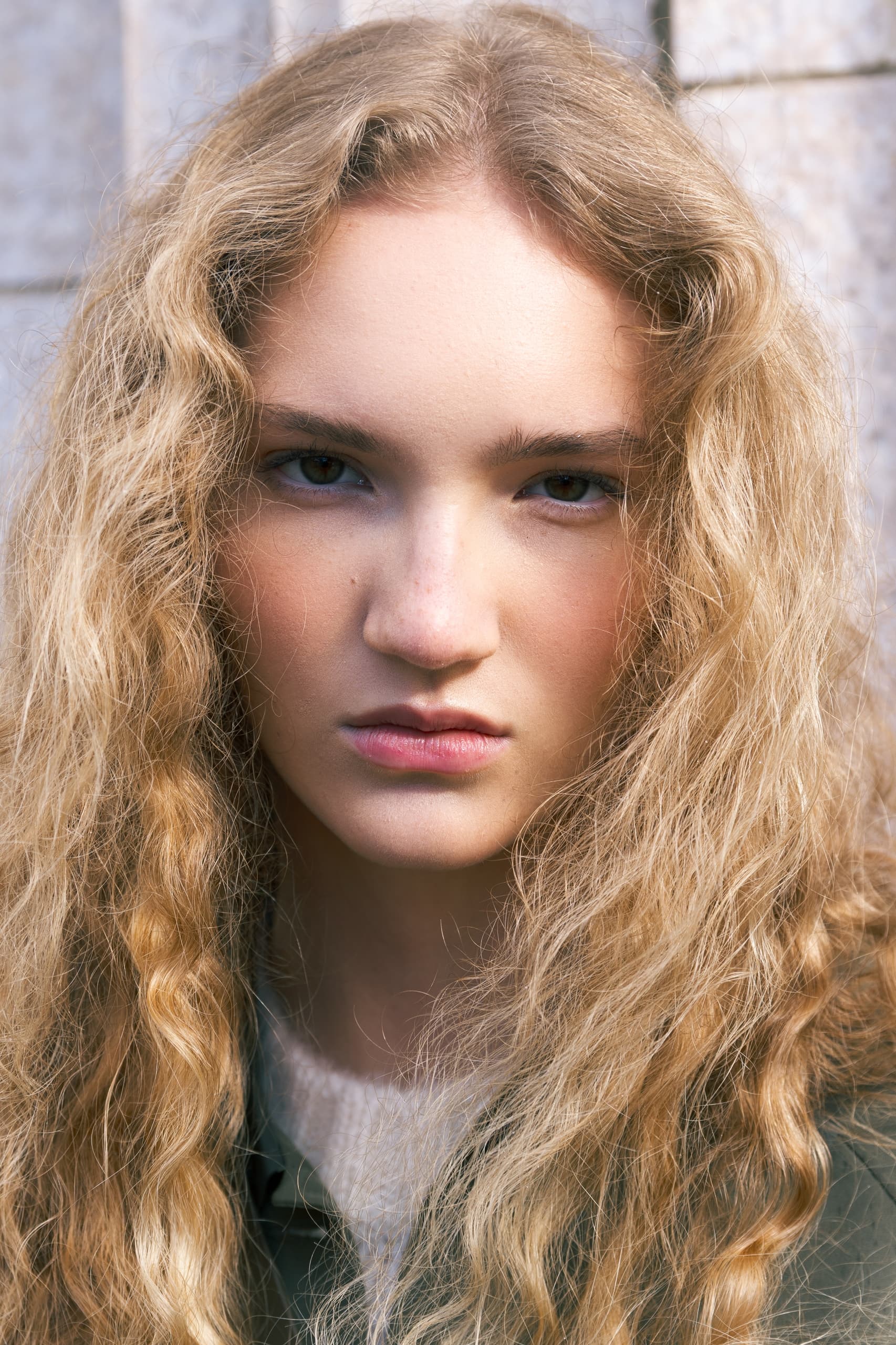 Portrait of a person with curly blonde hair against a textured background.