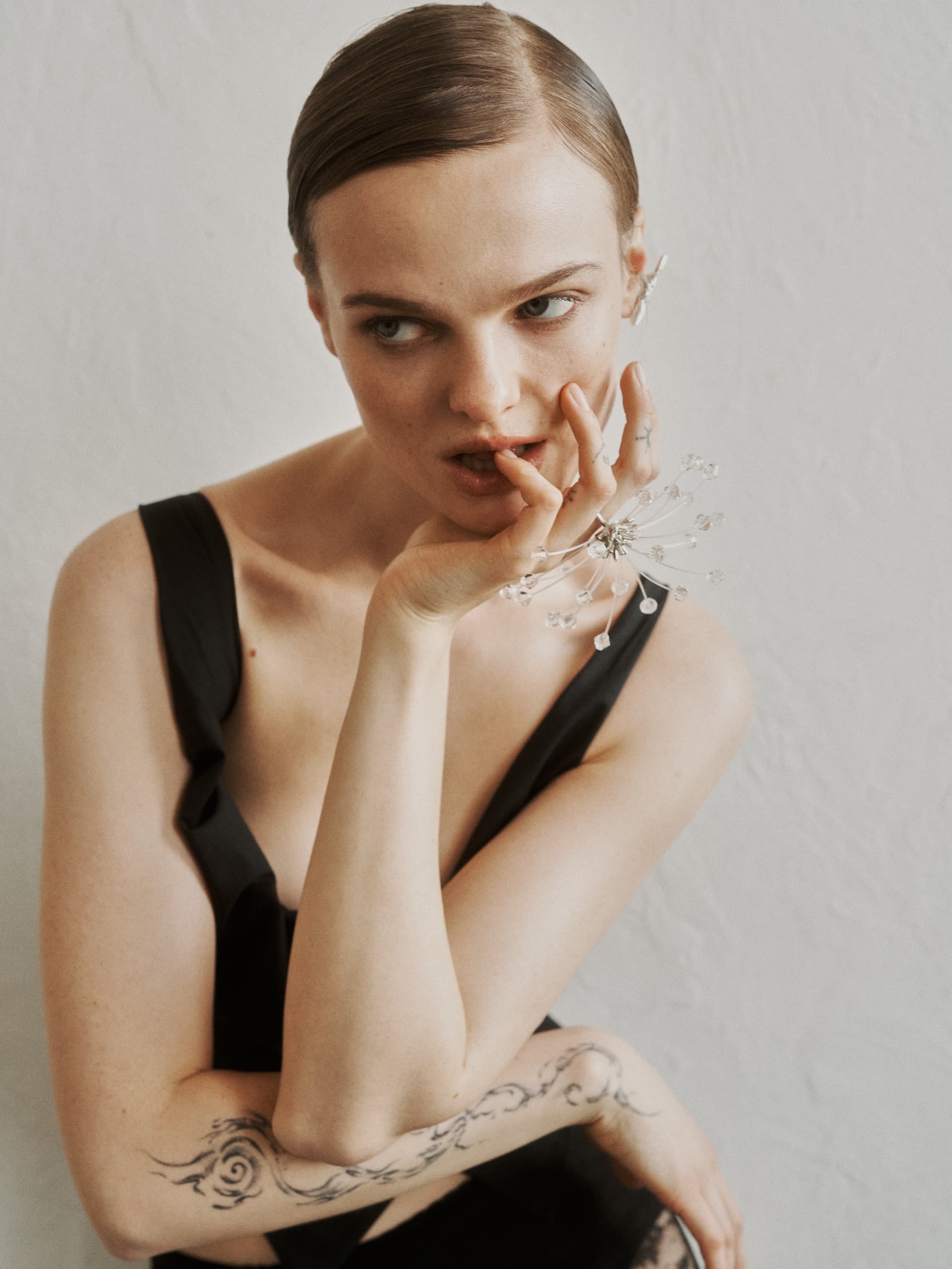 Model in elegant black dress with artistic hand pose and intricate jewelry.