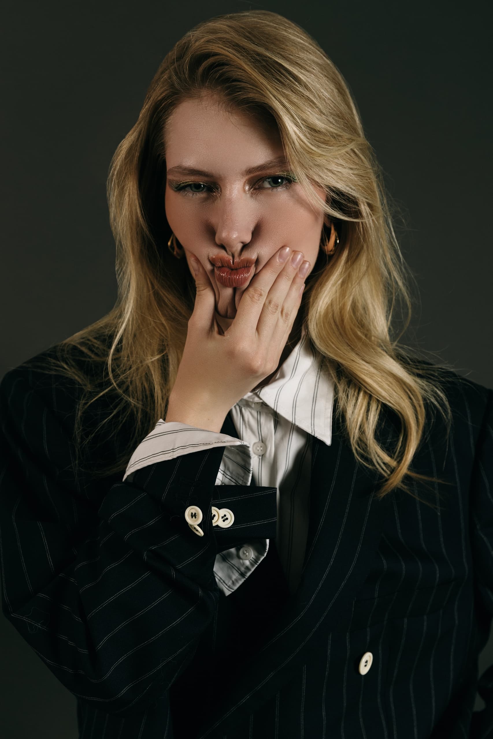 Woman in pinstripe suit making a playful face, hands on cheeks.