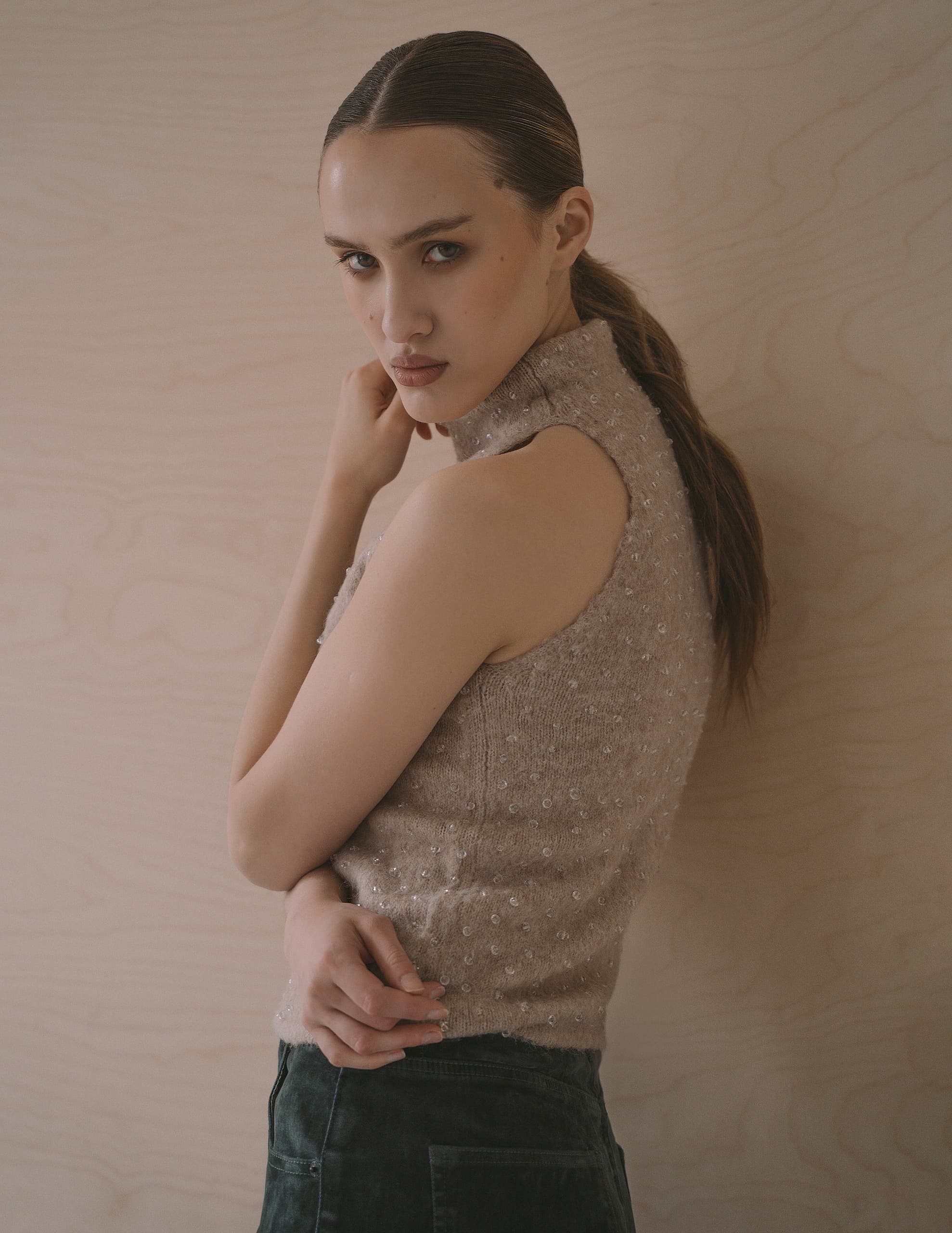 Woman in sleeveless top poses against a wooden wall.