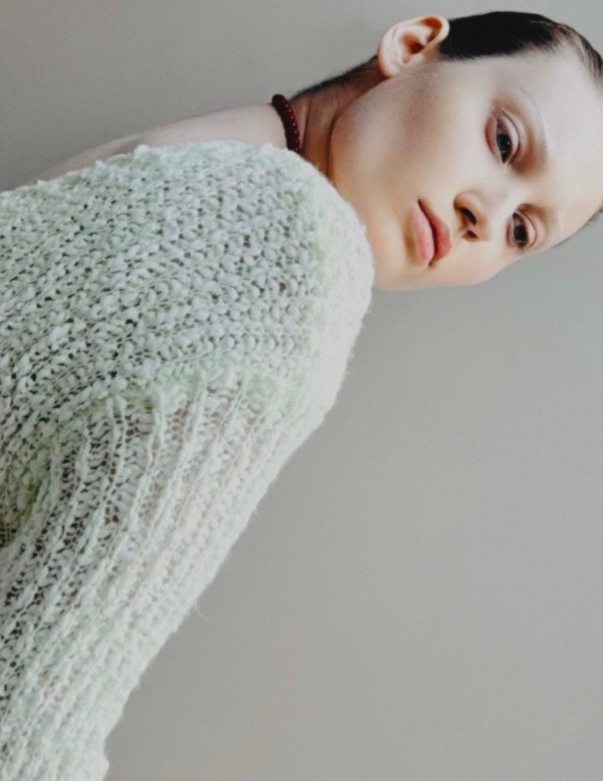 Person in textured sweater looking over shoulder against neutral background.