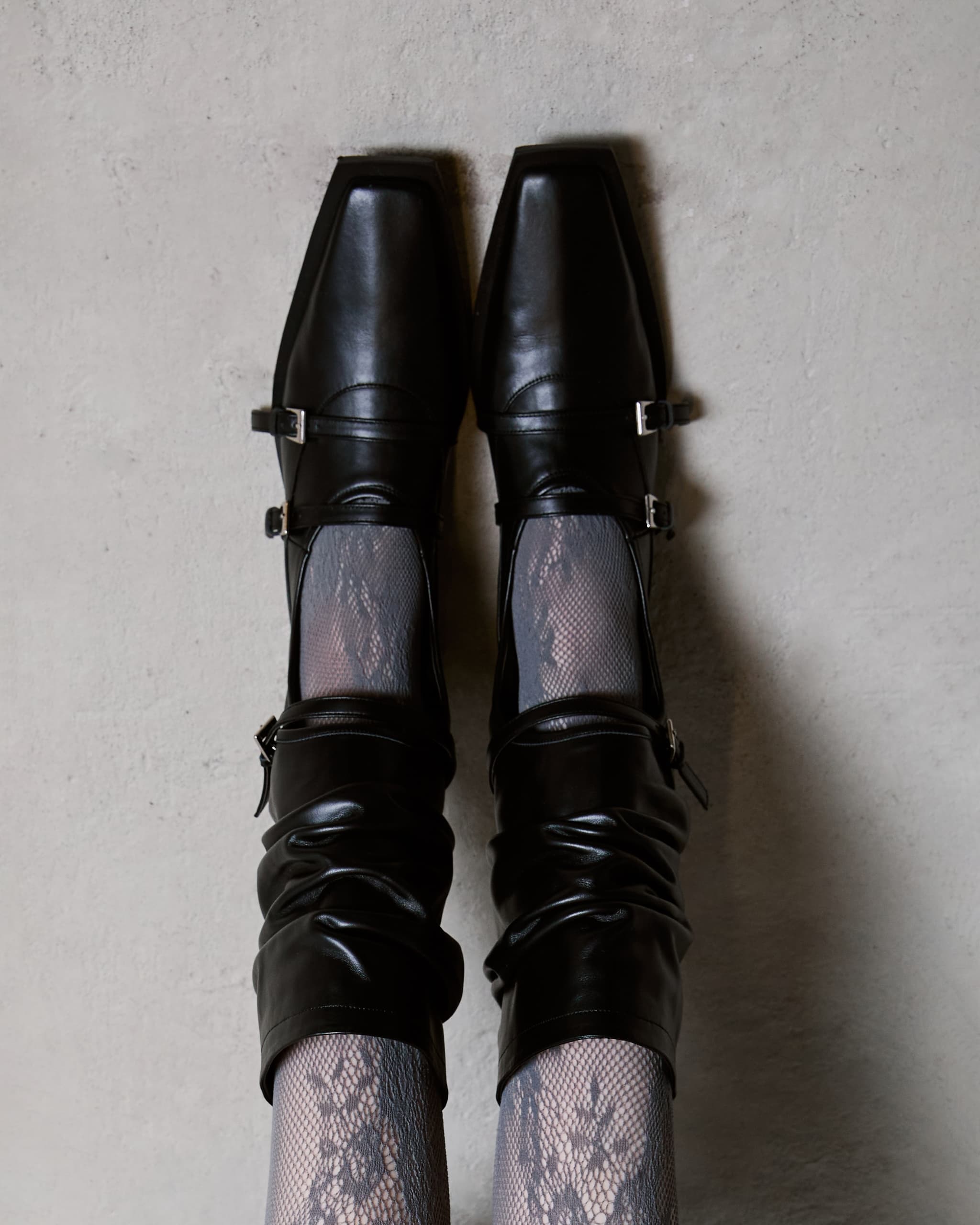 Black leather shoes with square toes and lace-patterned tights on a gray background.