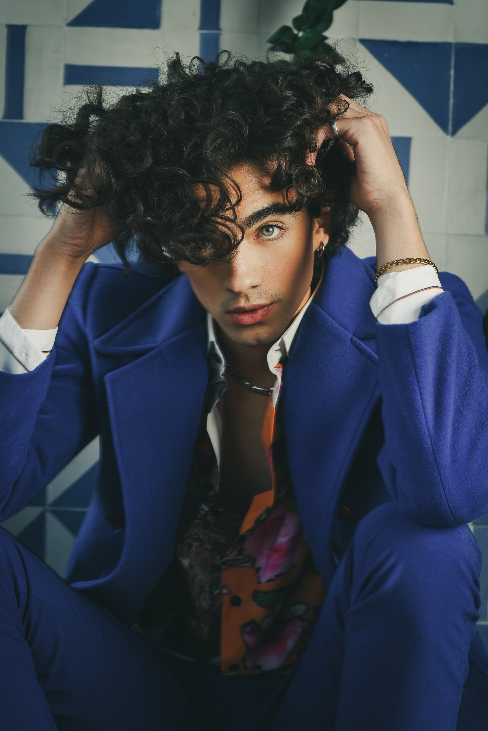 Person in vibrant blue suit seated with hands in curly hair.