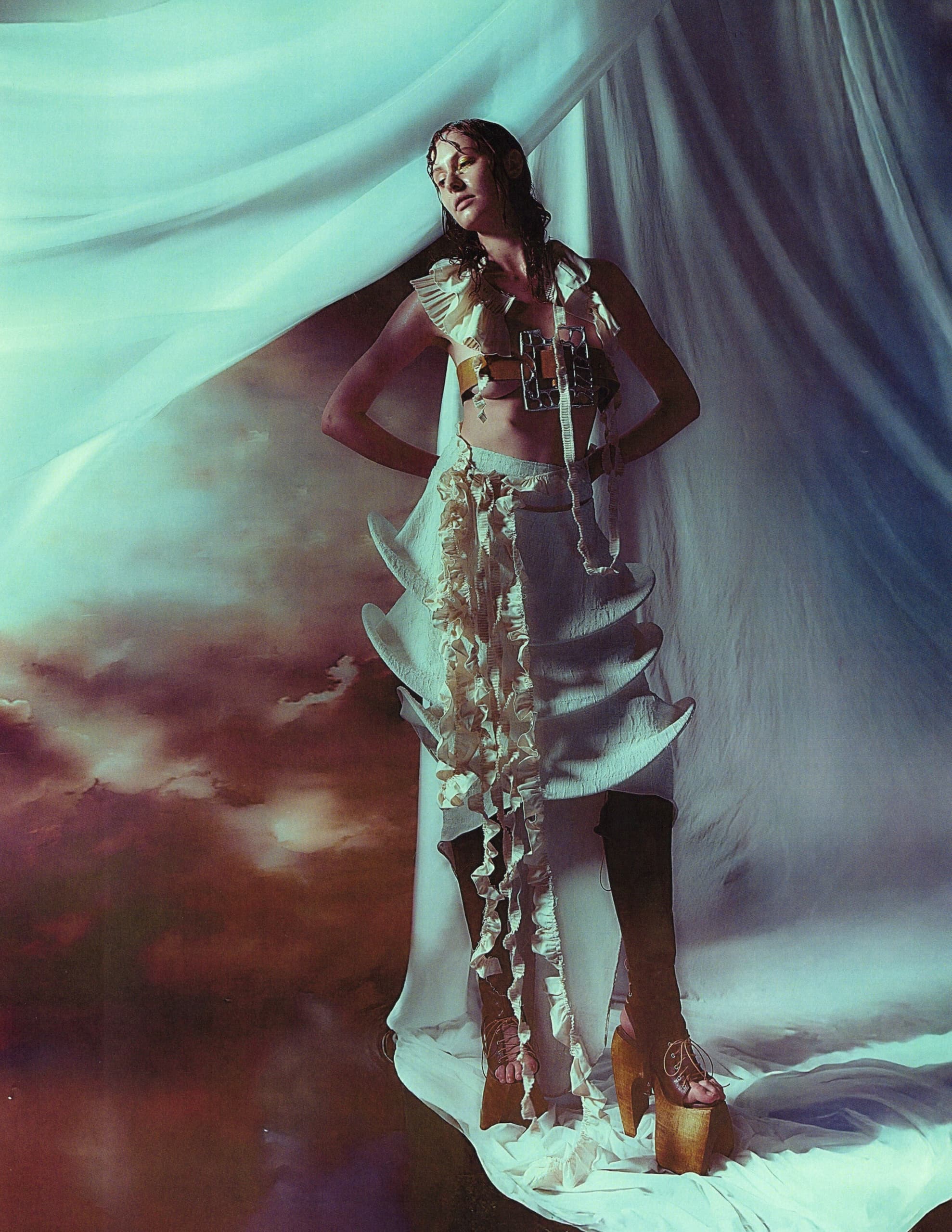 Fashion model in avant-garde outfit with flowing drapes and artistic lighting.
