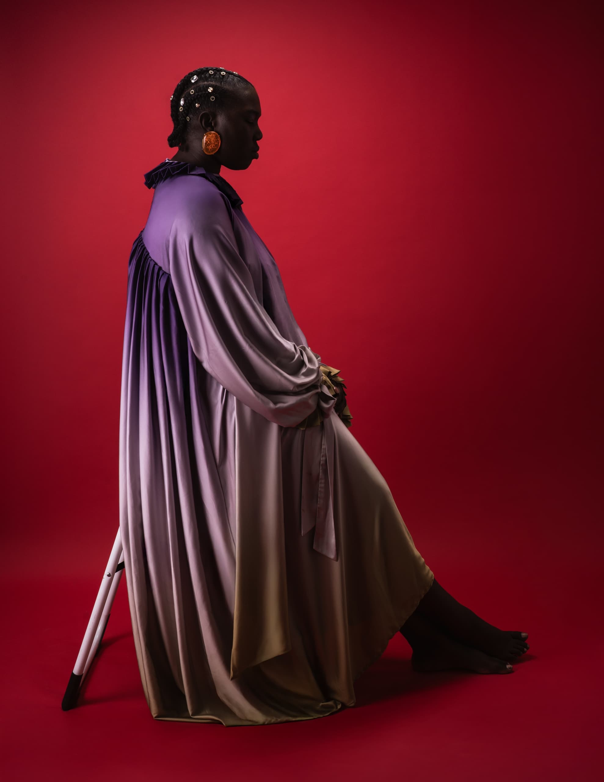 Elegant person in purple gown seated against a vibrant red backdrop.