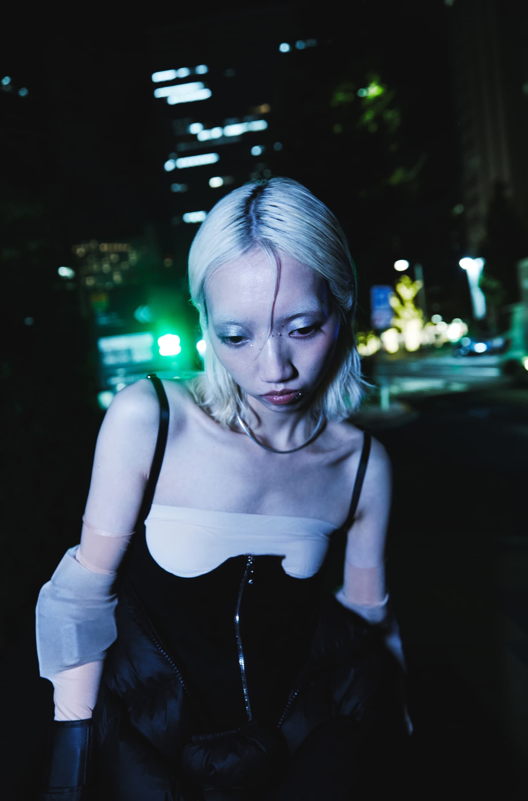 Fashionable person with blonde hair and stylish outfit in a city night scene.