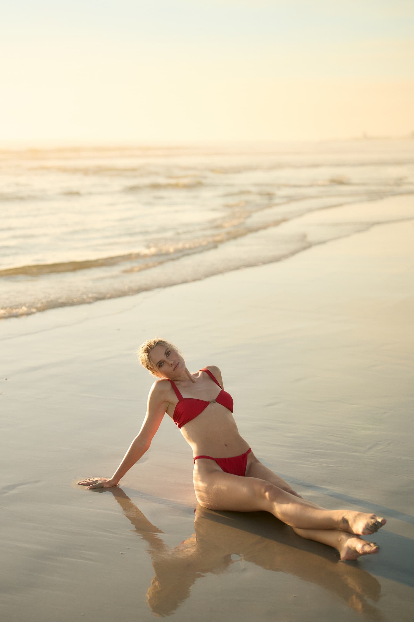 Person in red bikini relaxing on the beach at sunset, serene ocean backdrop.