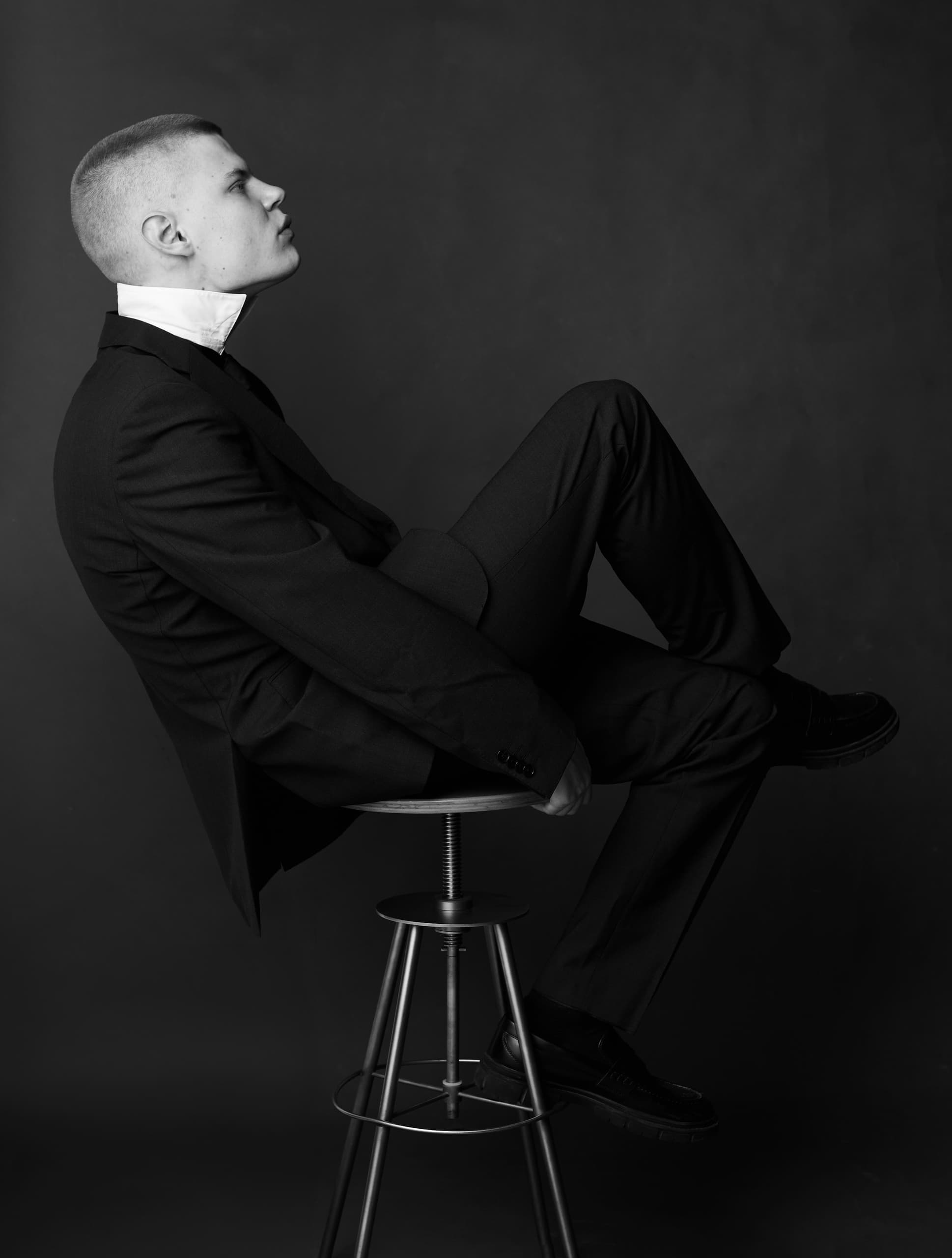Man in a suit sitting stylishly on a stool, black and white portrait.