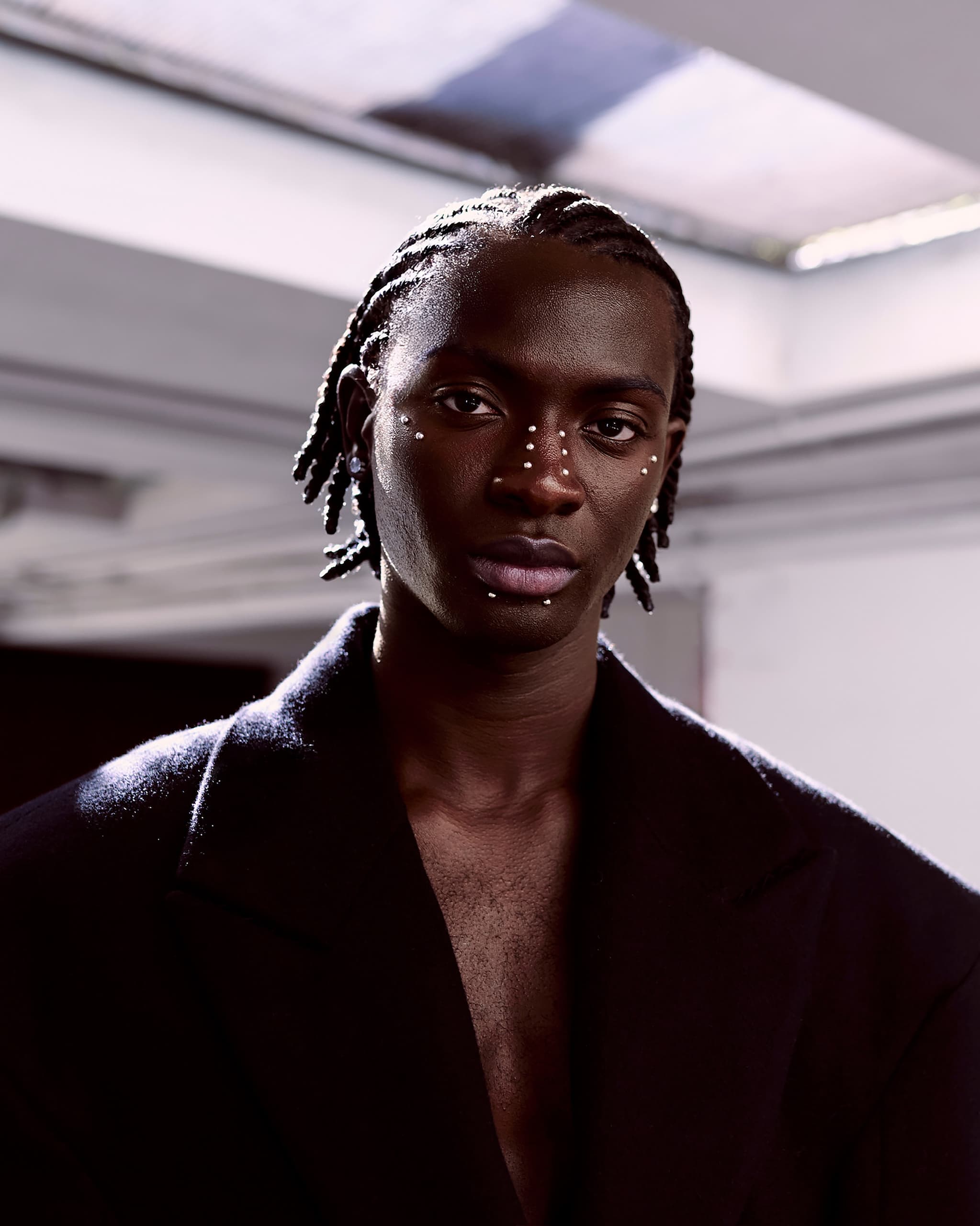 Person wearing a dark coat with decorative face accents in artistic lighting.