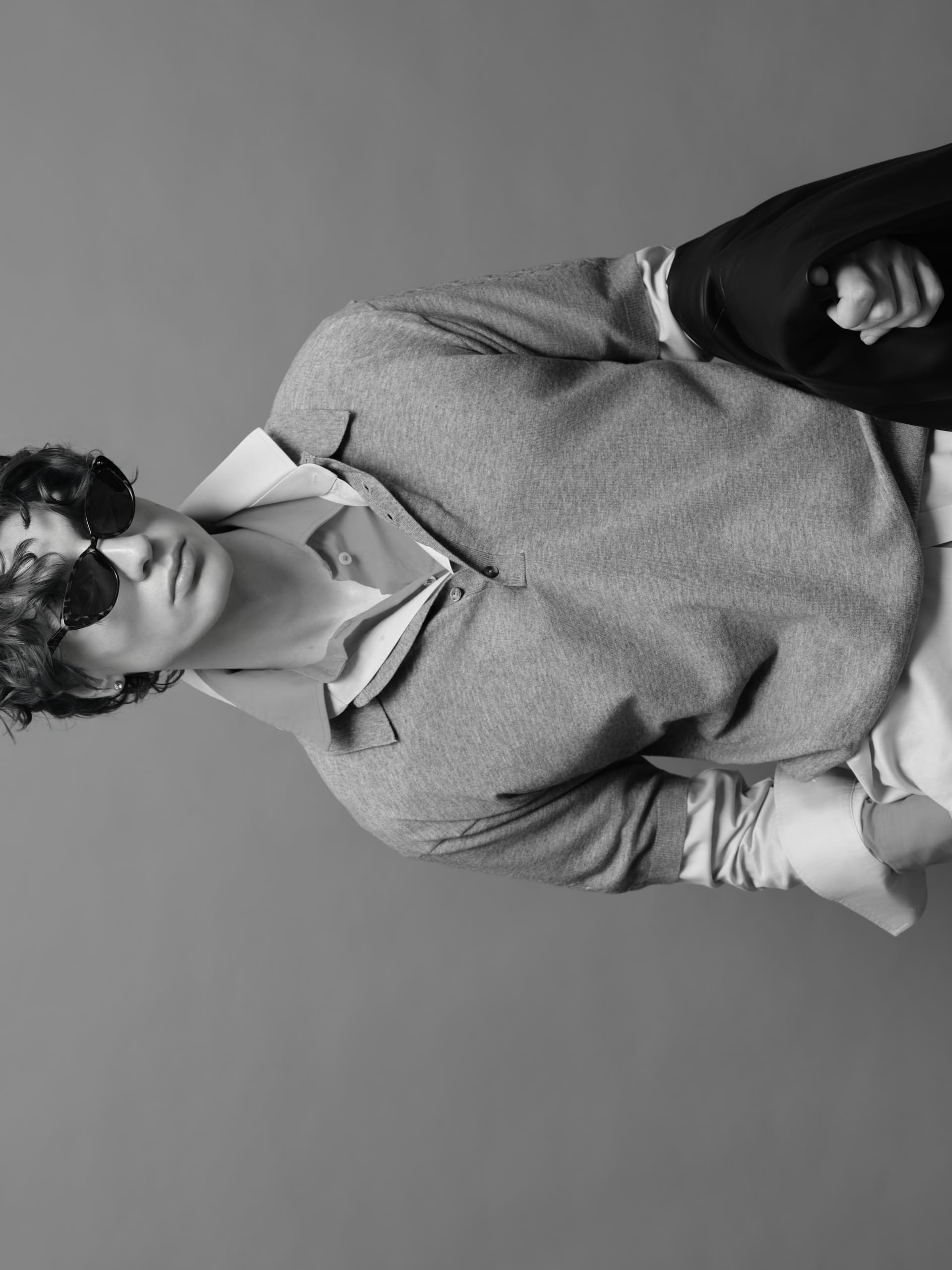 Stylish person in sunglasses wearing layered clothing, carrying a jacket.