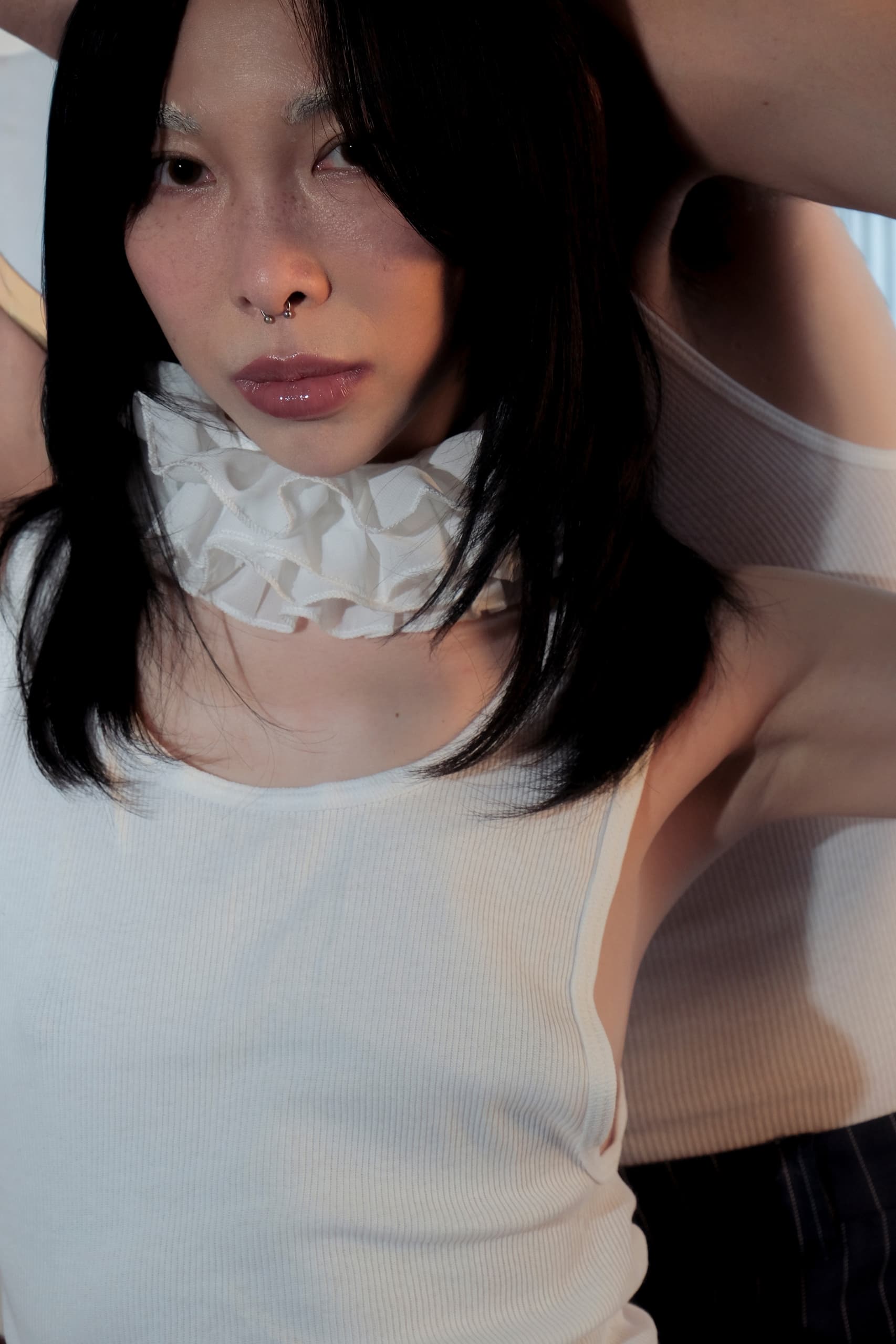 Person wearing white top and ruffled collar with serious expression.