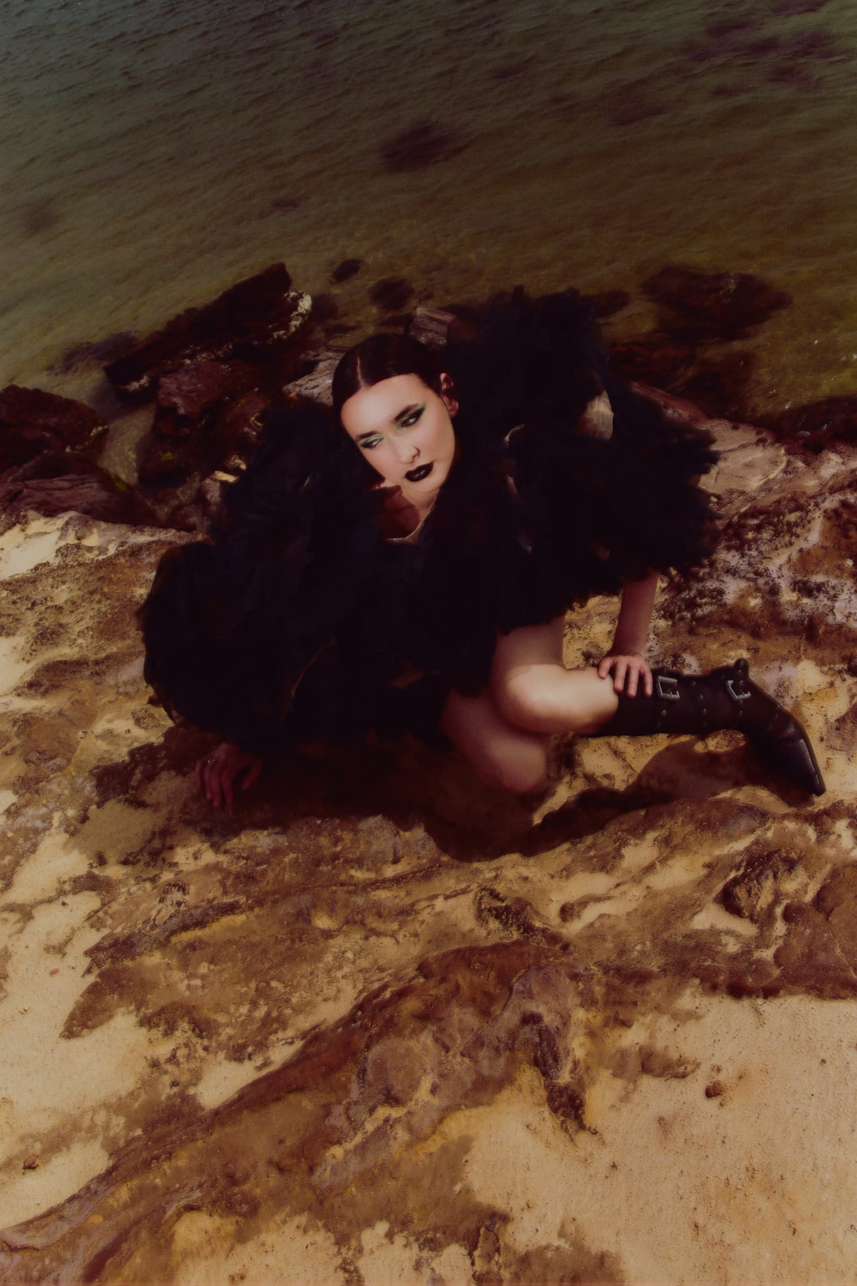 Fashion model in dramatic black outfit posing on a rocky beach.