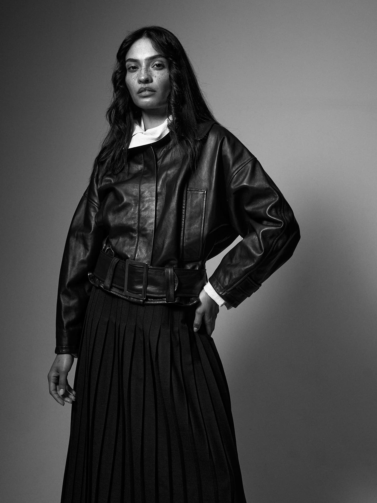 Black and white fashion shot of a woman in a leather jacket and pleated skirt.