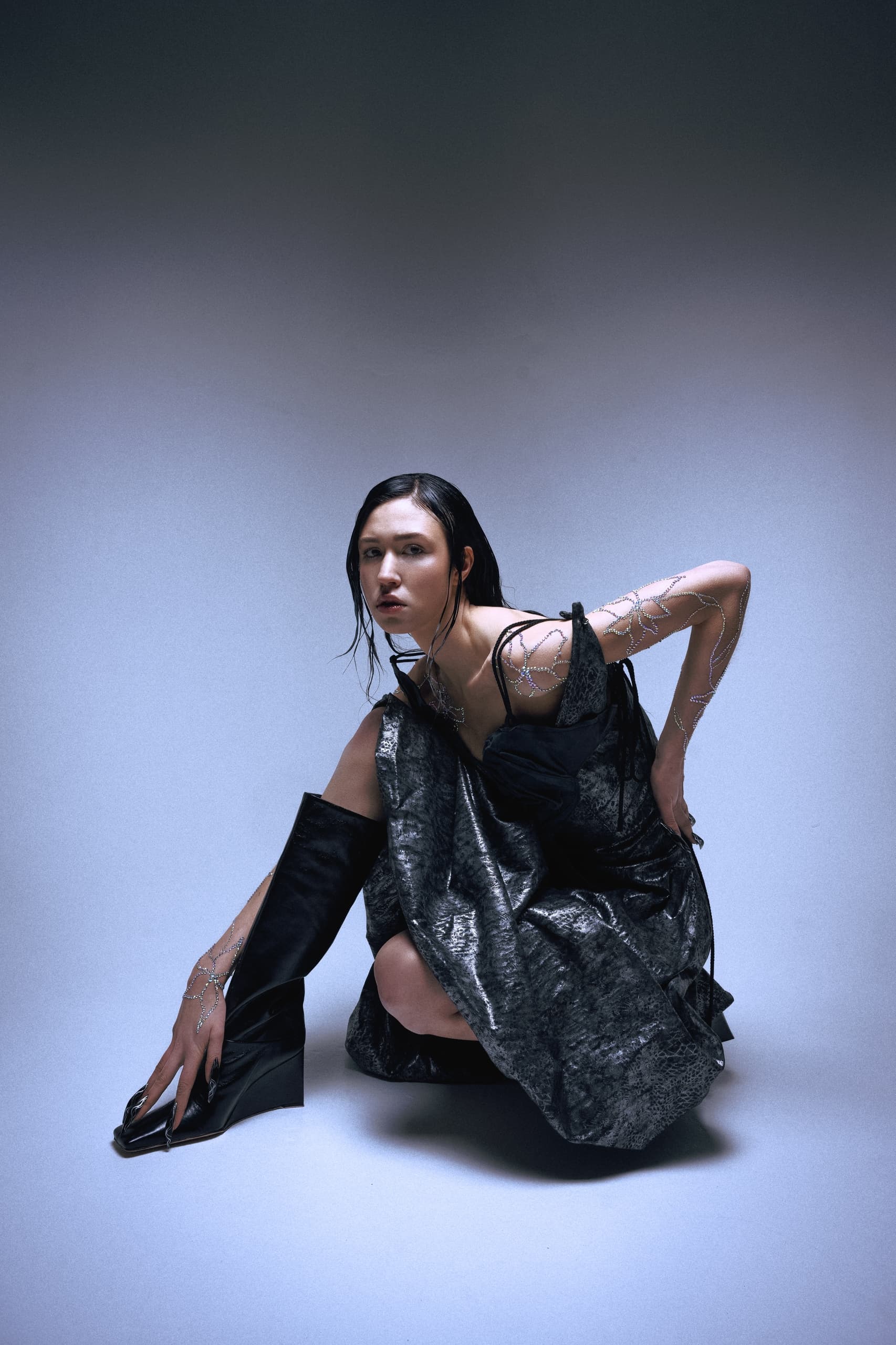 Fashion model posing in futuristic black and silver outfit with artistic arm designs.