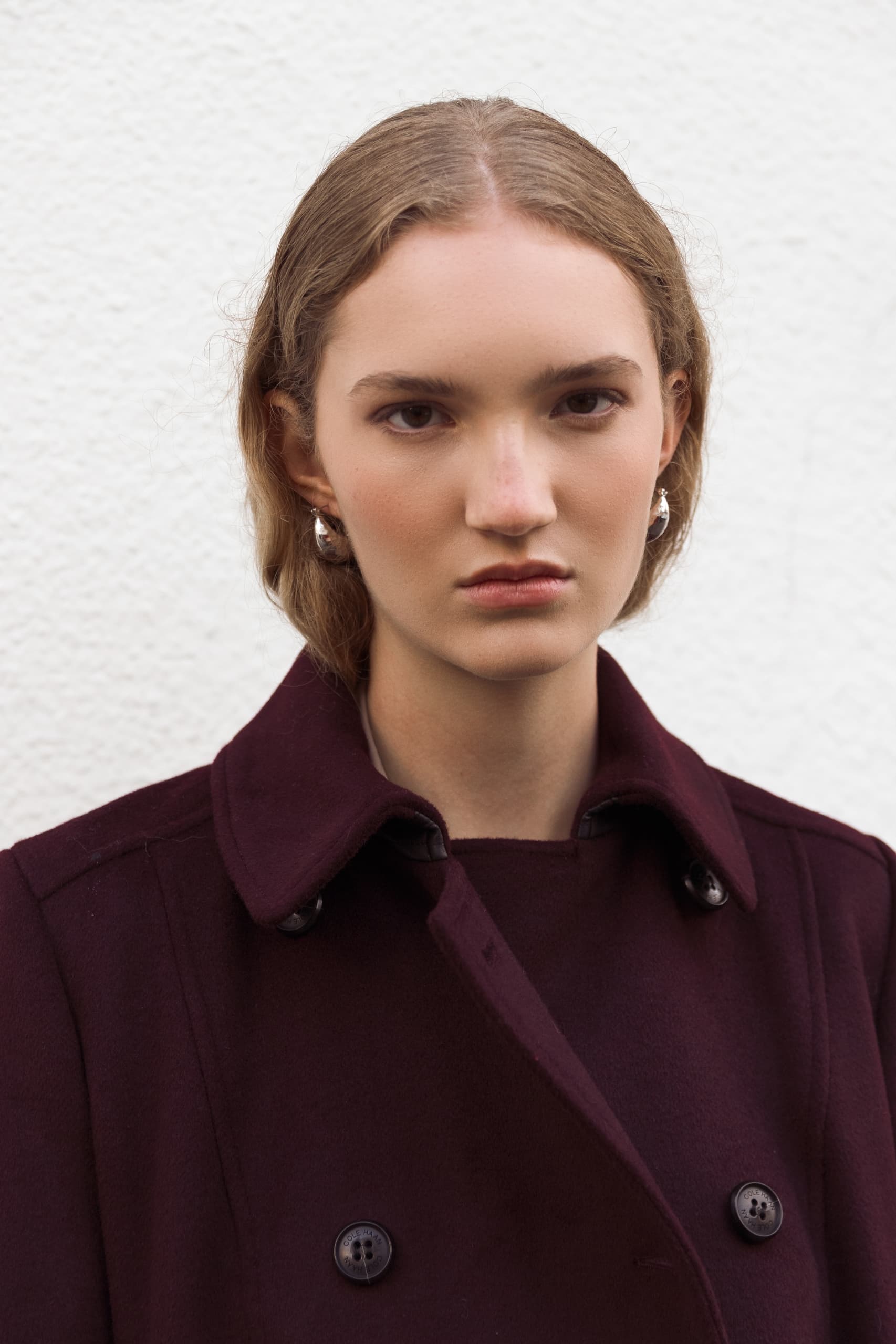Person wearing maroon coat standing against a white textured wall.
