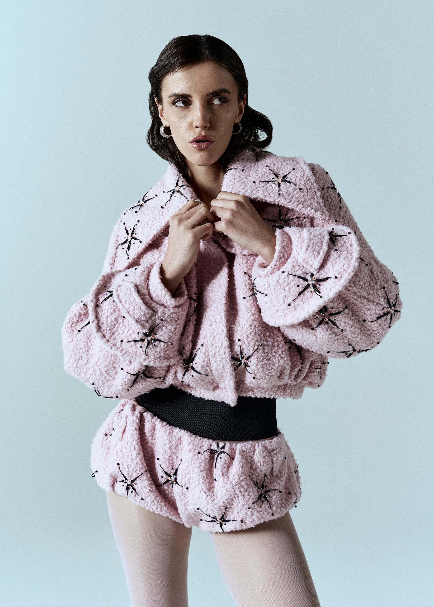 Model in pink textured jacket and shorts poses against a neutral background.