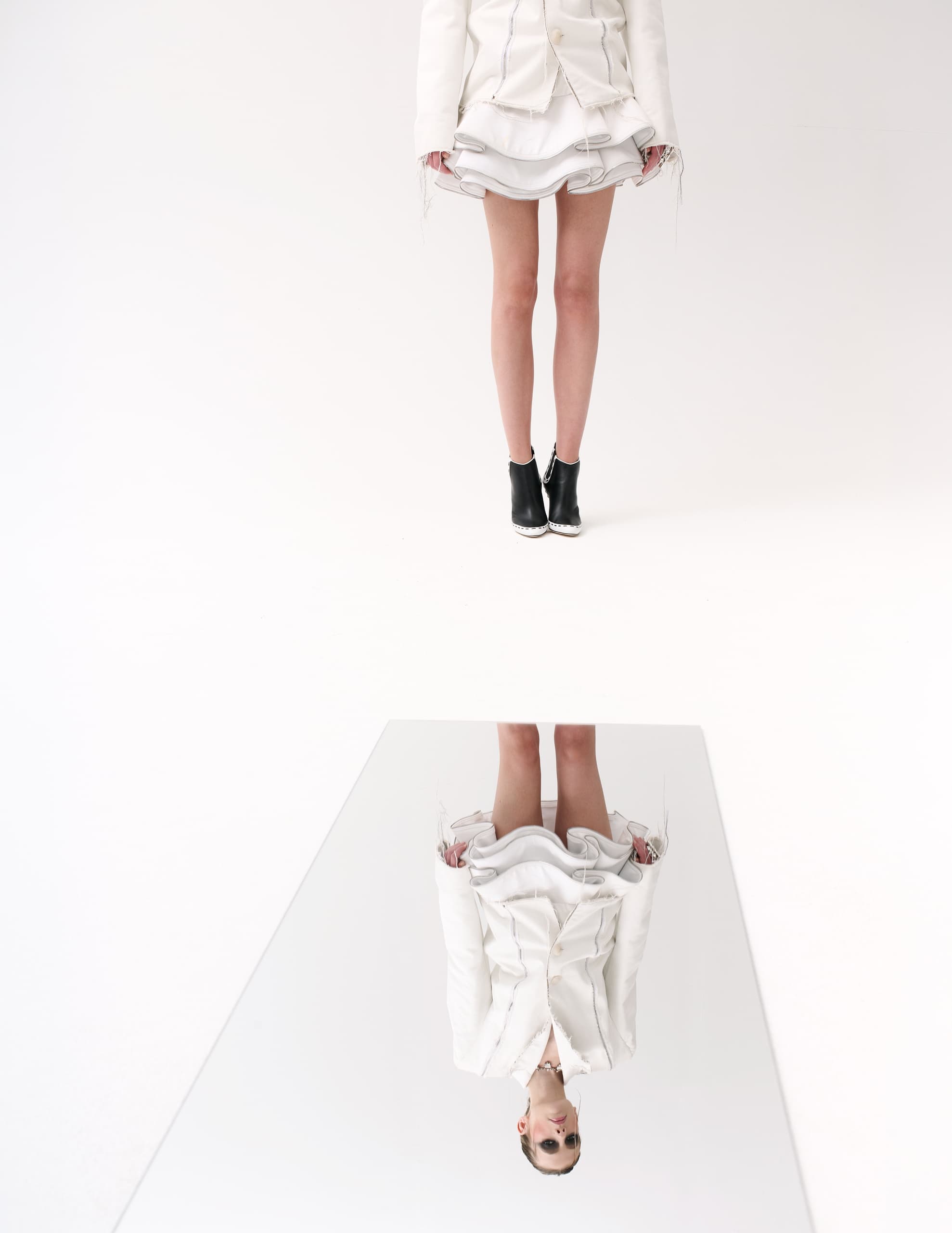 Fashion model in white outfit mirrored on the floor. Black boots accent the look.