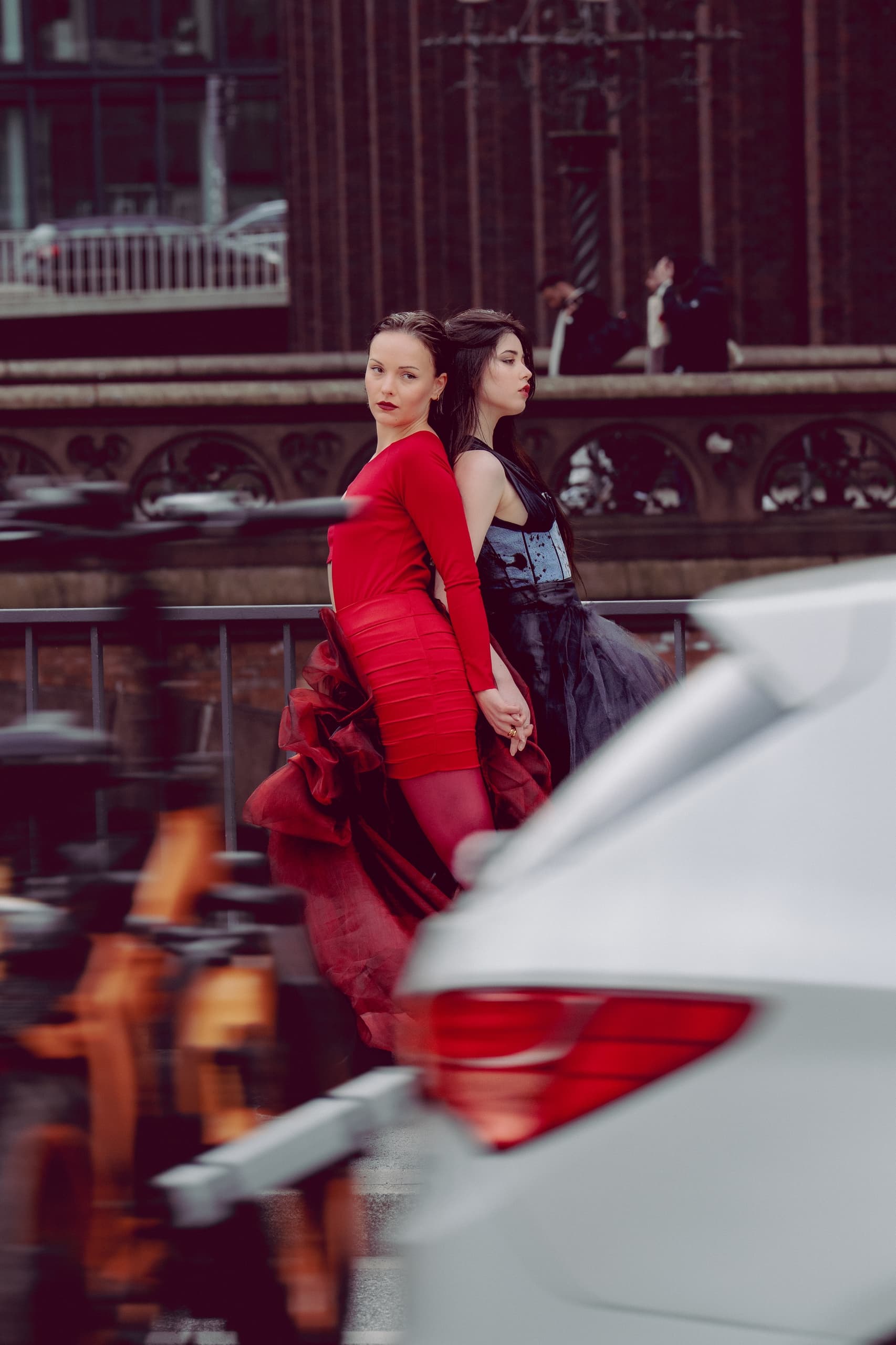 Two women in vibrant dresses pose on a city street, with blurred motion in foreground.