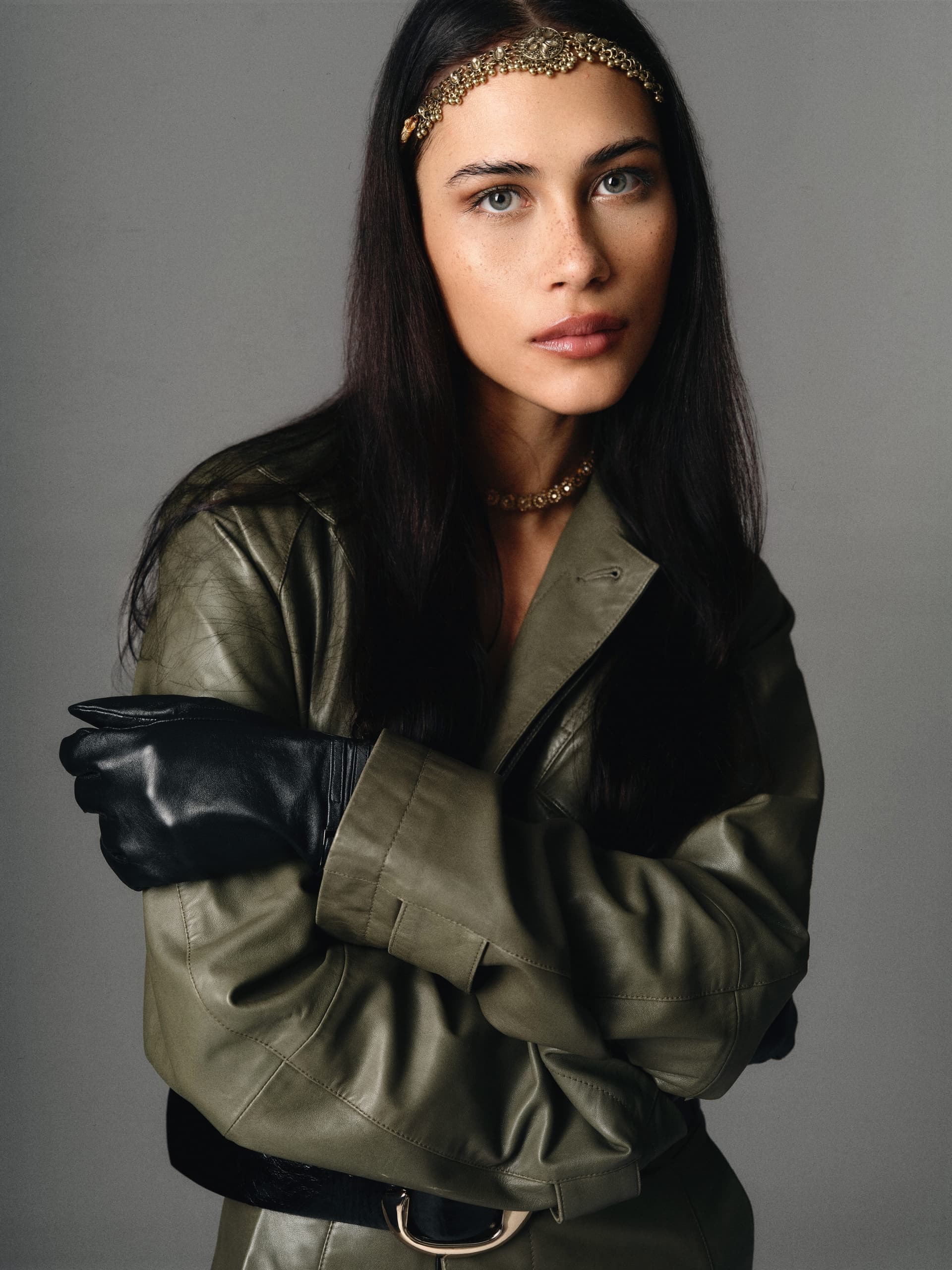 Elegant woman in olive jacket with black gloves and ornate headband.