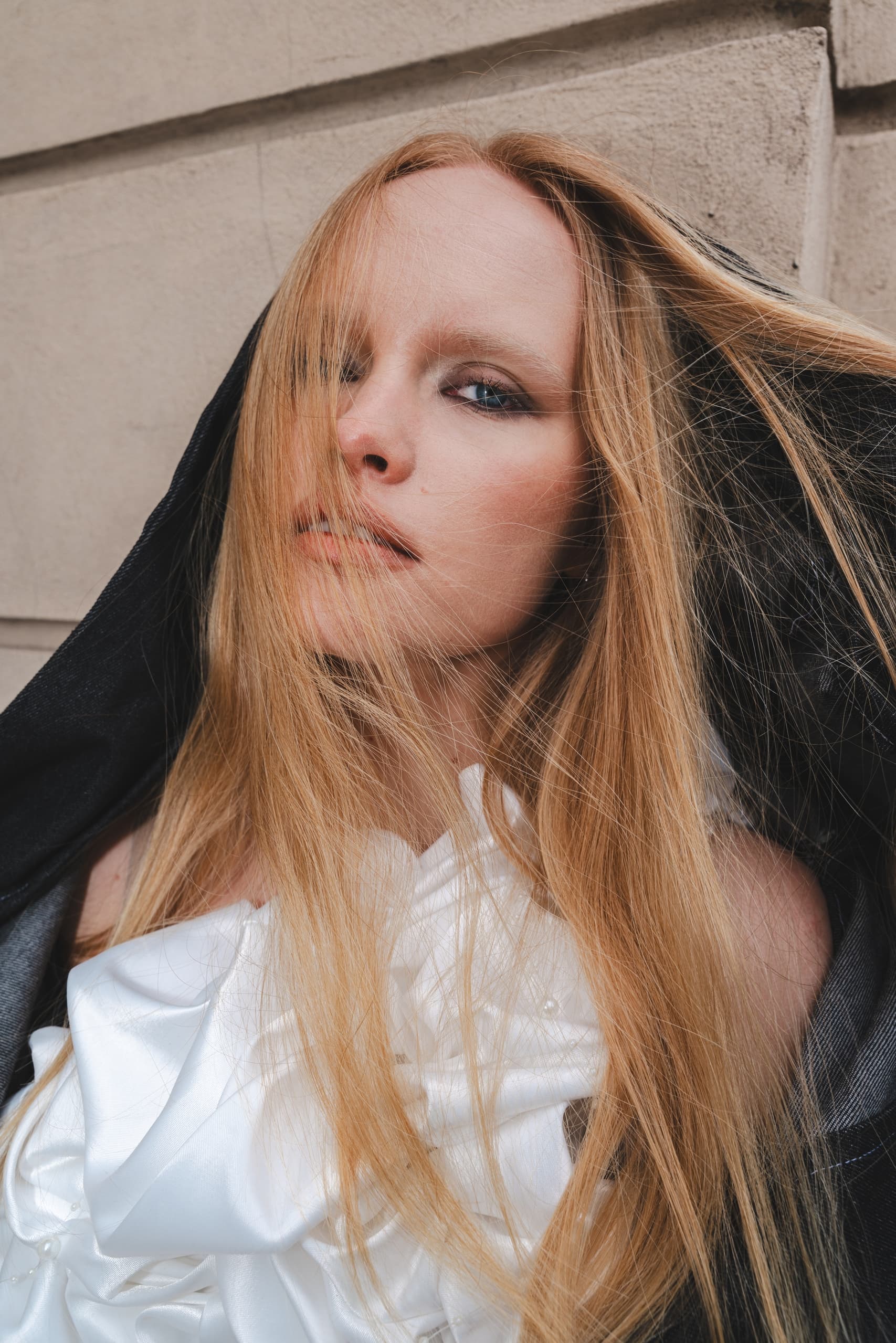 Model with long blonde hair in stylish black hooded outfit.
