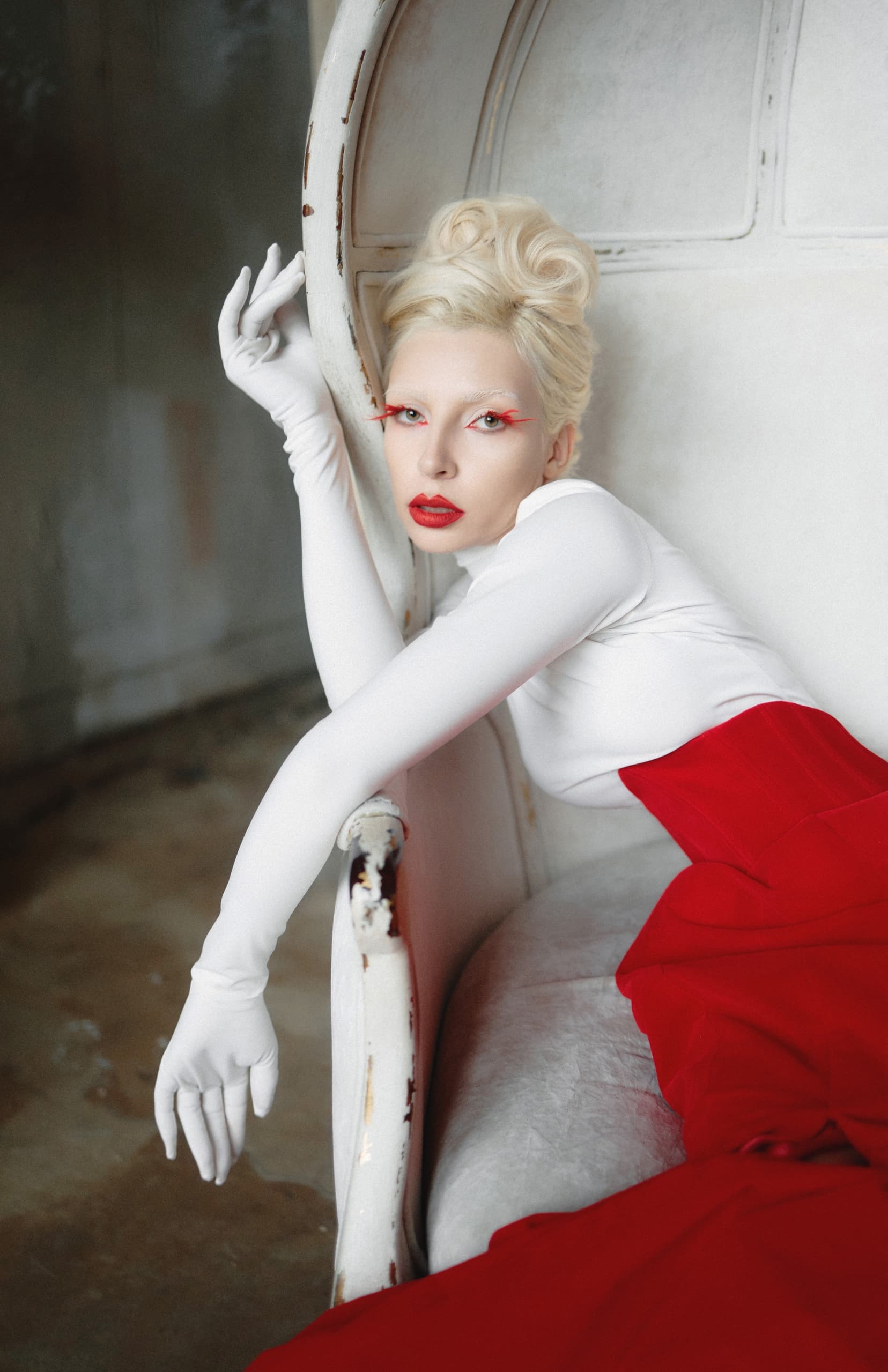 Elegant model in red and white fashion, striking pose on vintage chair.