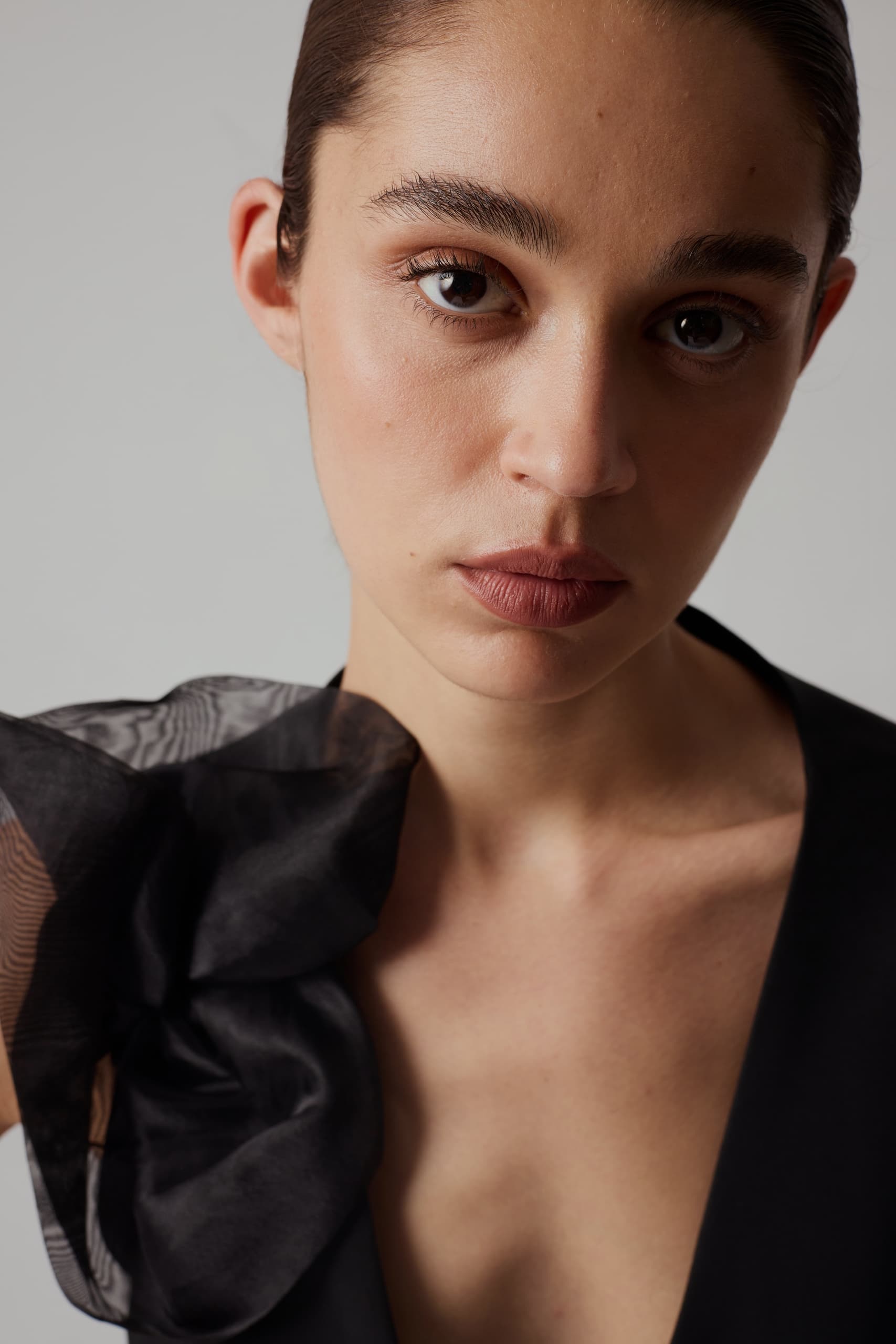 Elegant woman in black dress with floral shoulder detail, close-up portrait.