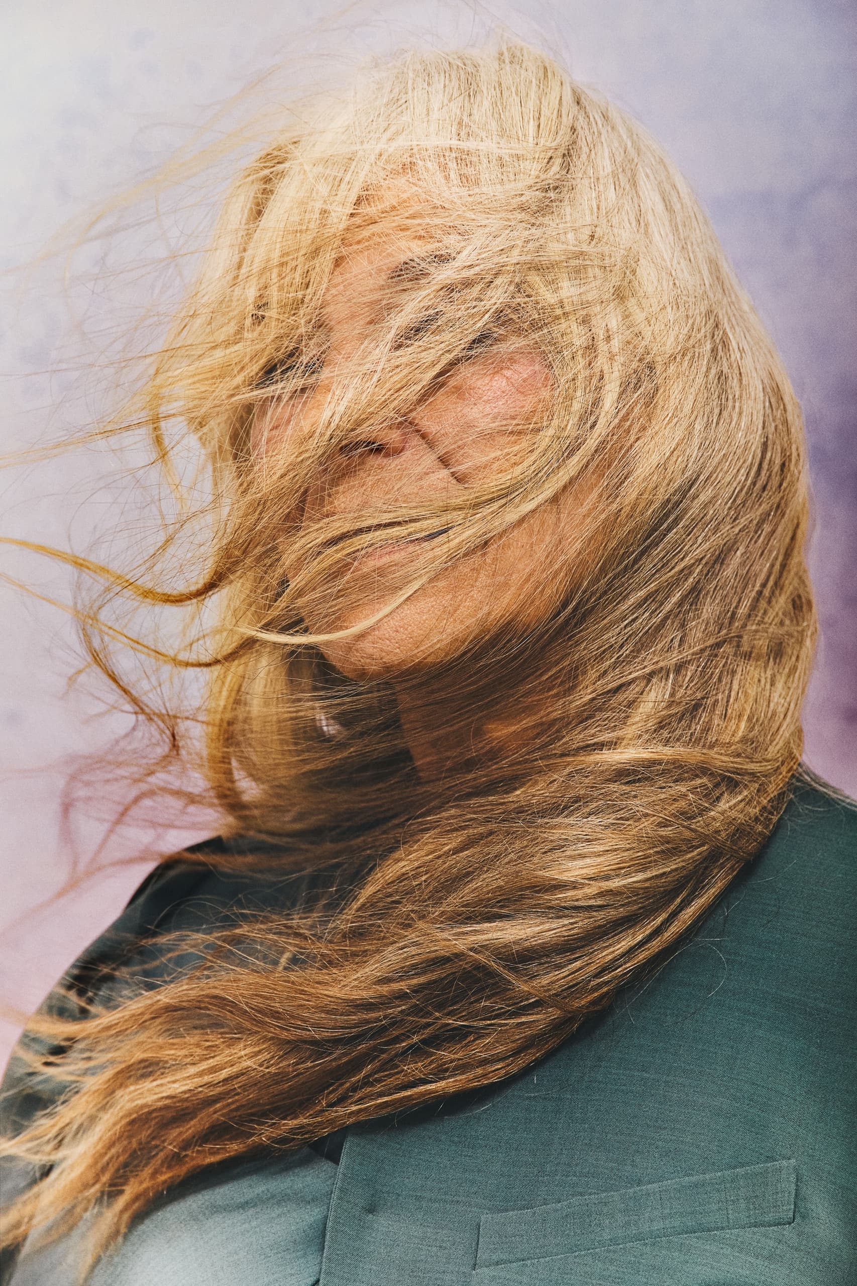 Woman with windswept hair and teal coat against a pastel background.