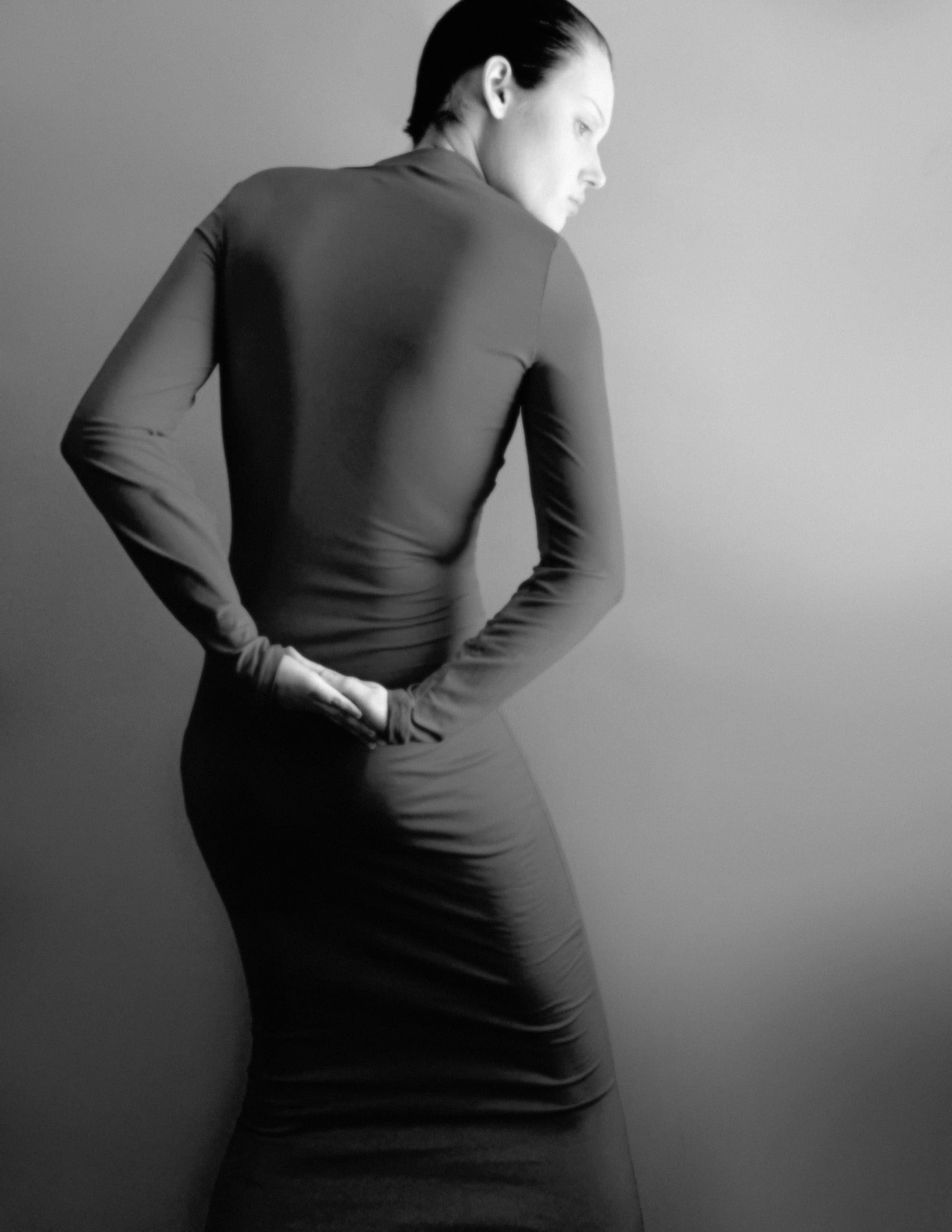 Elegant silhouette of a woman in a long dress, posing against a grey background.