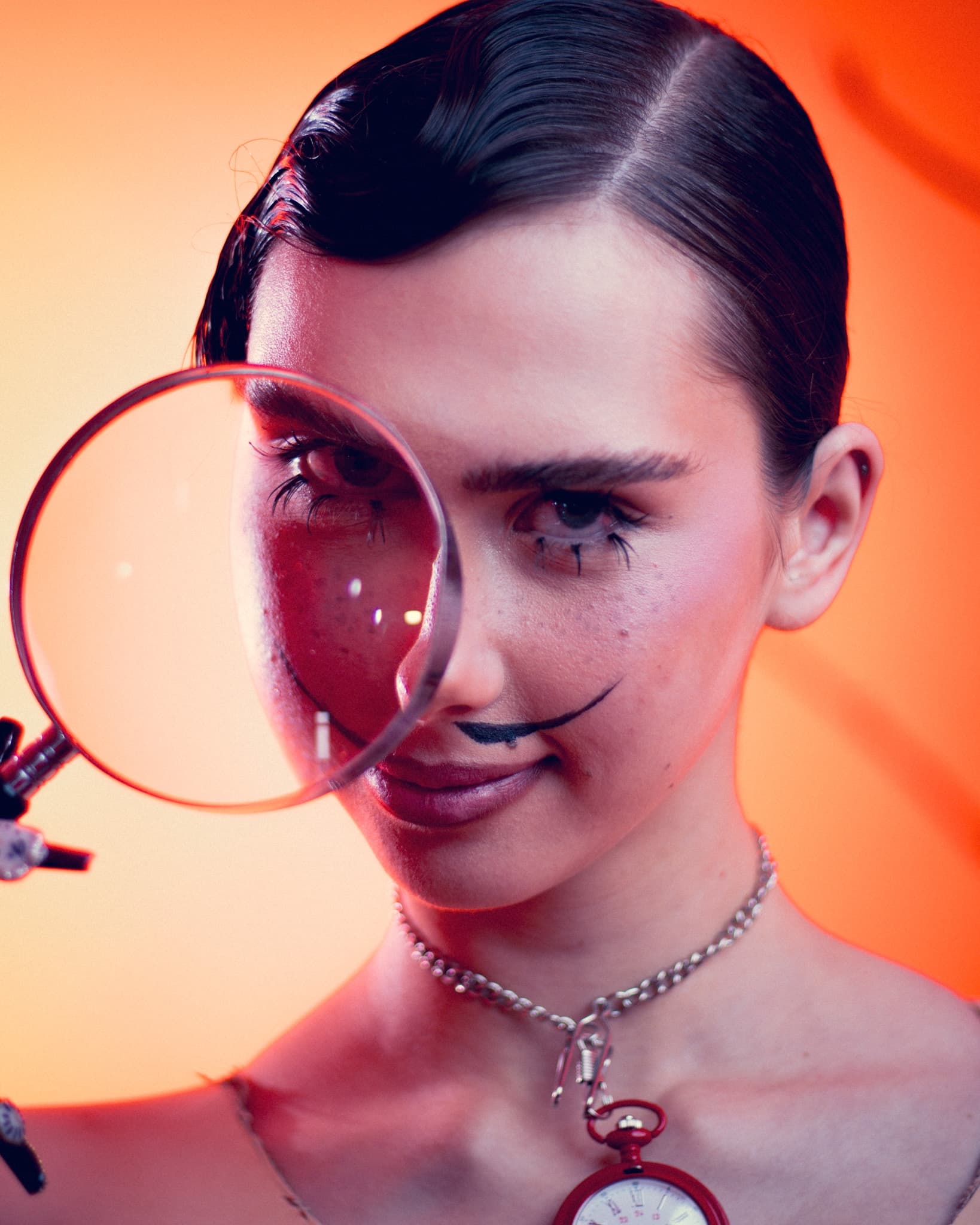 Woman with vintage style makeup holding magnifying glass, surreal orange backdrop.