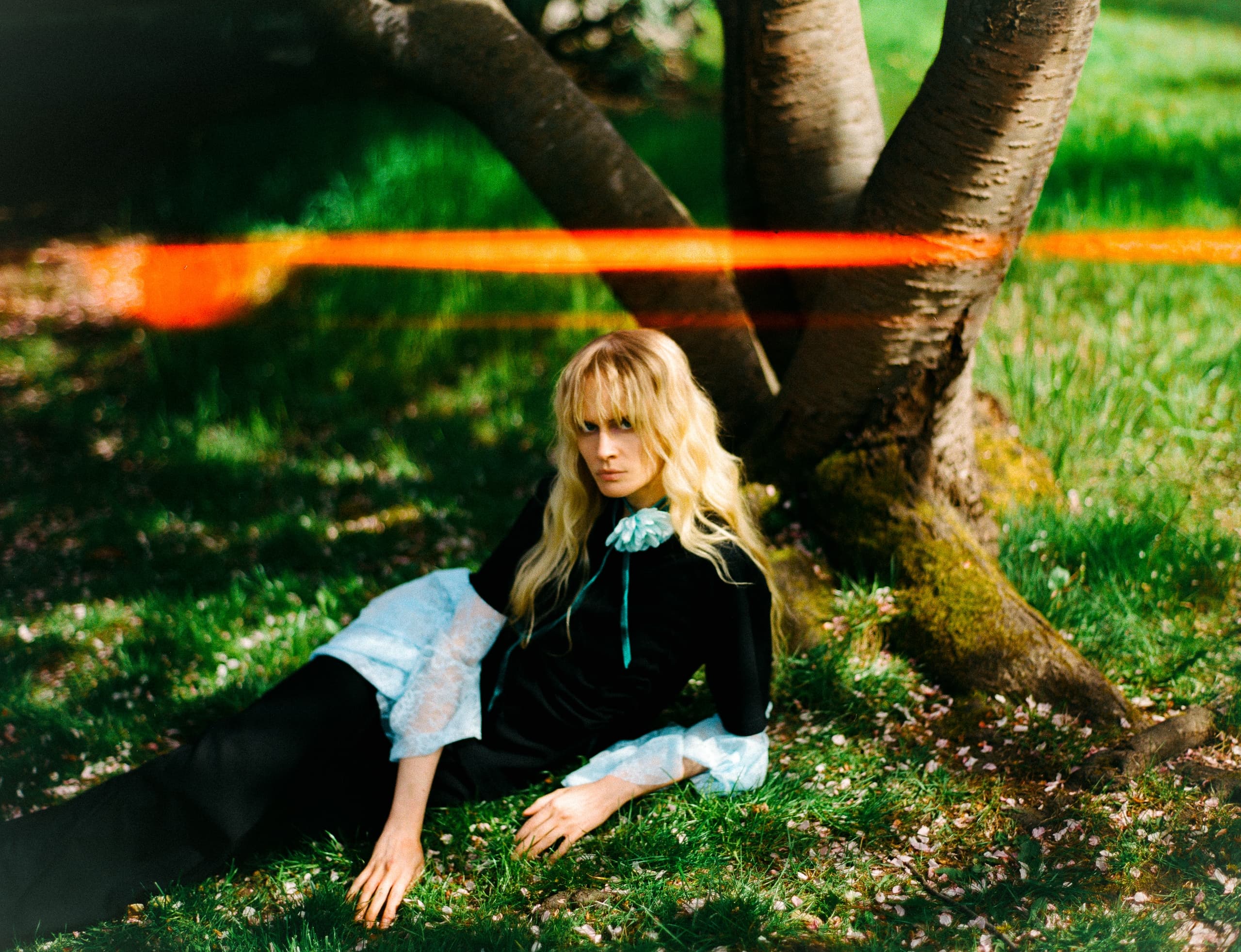 Woman in vintage black dress relaxing under tree with vibrant green grass.