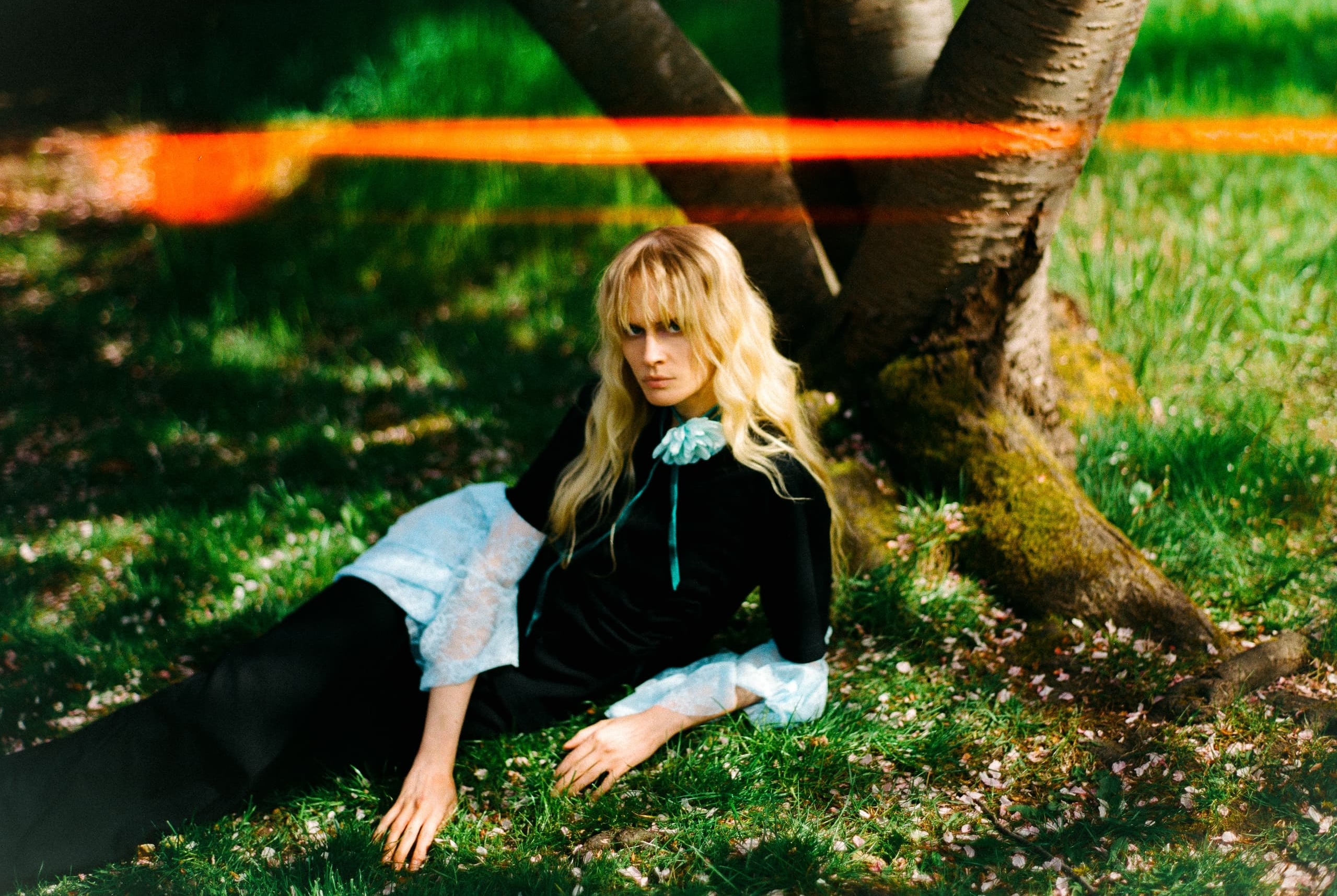Woman in stylish outfit sitting under a tree in a sunlit garden.