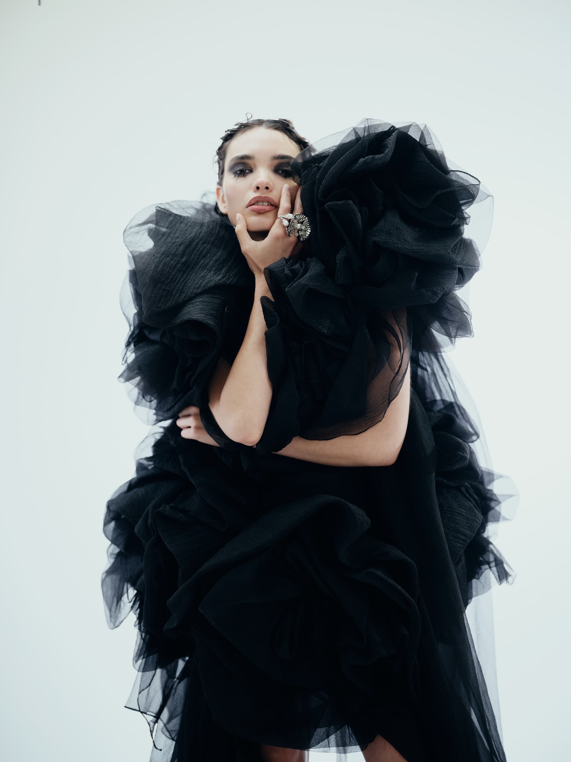Model in dramatic black ruffled dress on white background, fashion photography.