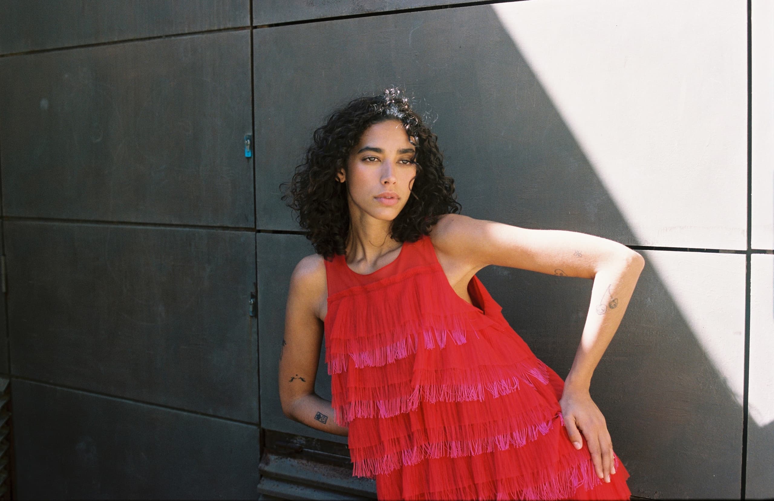 Woman in red fringed dress poses against geometric wall background.