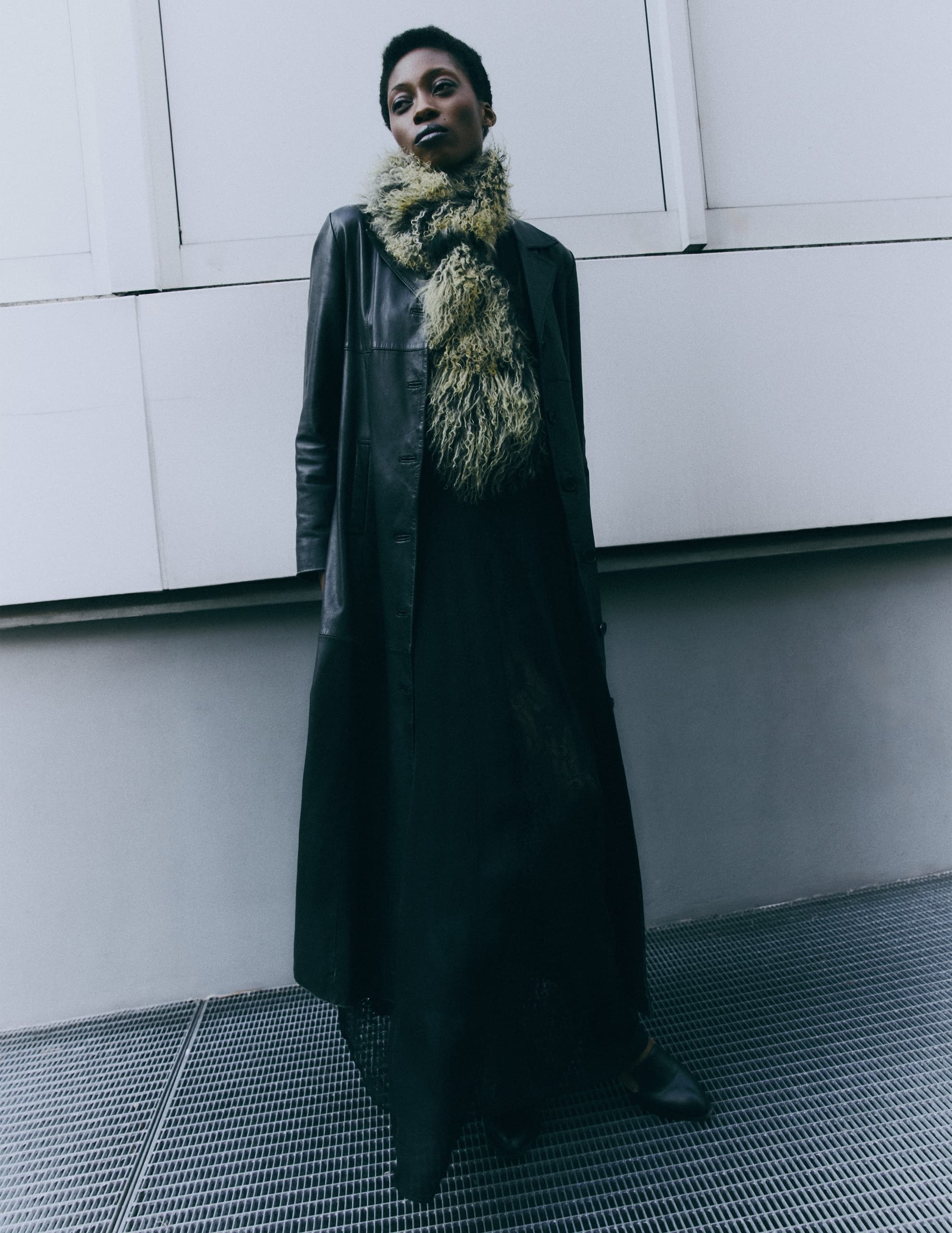 Stylish woman in black coat and fuzzy scarf, urban fashion photo.
