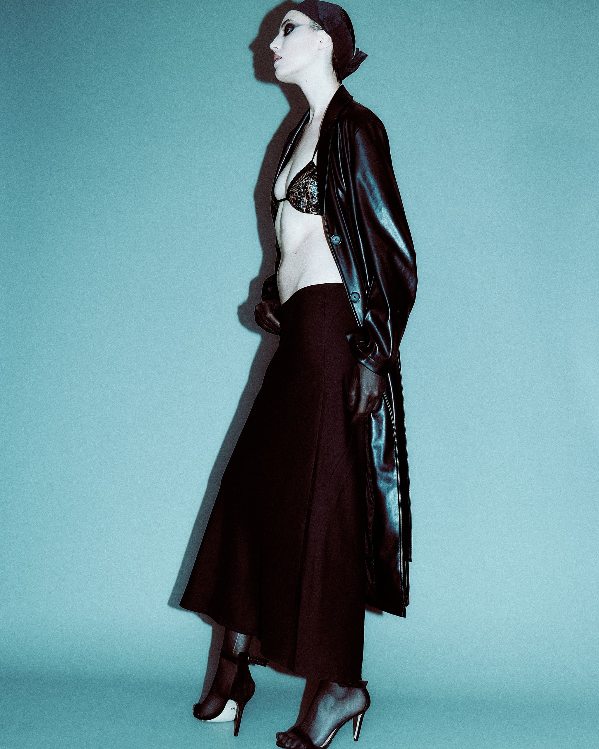 Fashion model in black outfit and heels, striking a side pose against blue background.