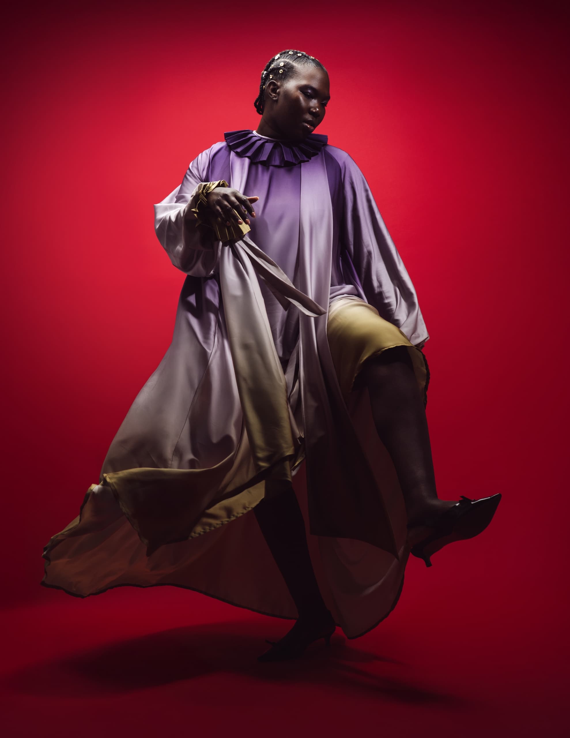 Person in elegant, flowing dress on bold red background, striking a dramatic pose.