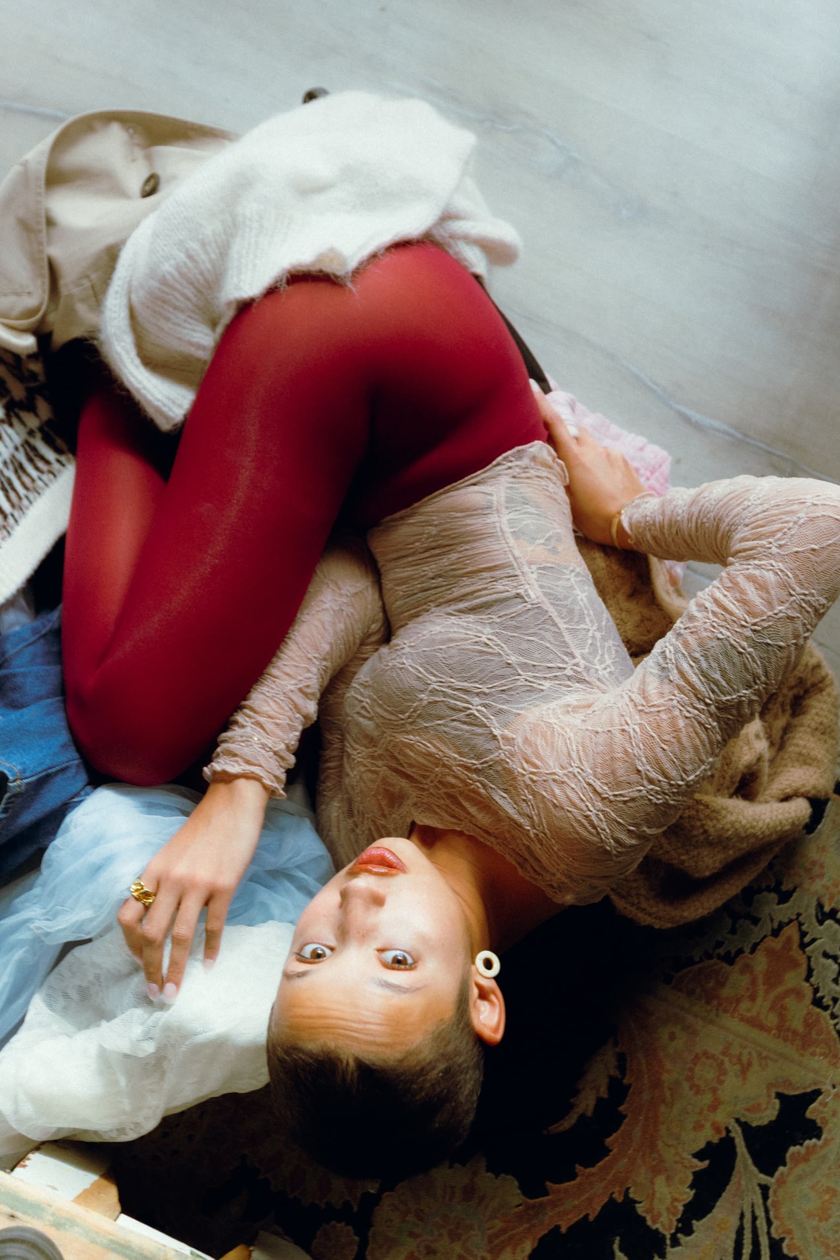 Person in red tights and sheer top relaxing on a patterned floor.