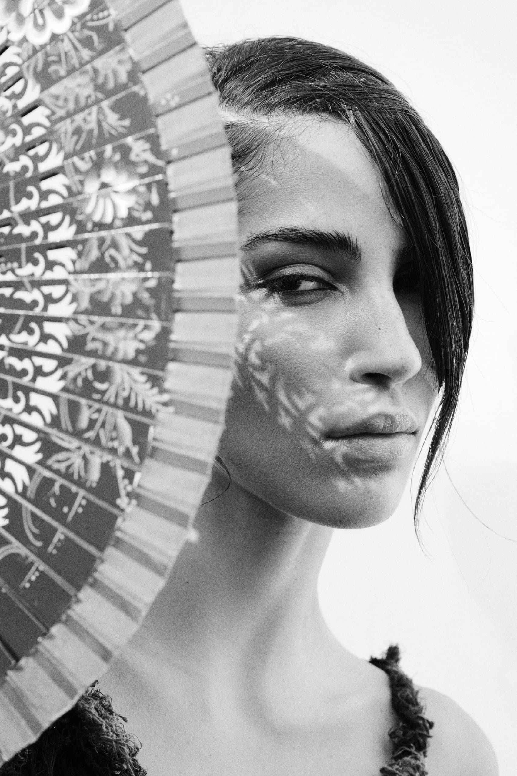 Black and white portrait with decorative hand fan shadow on face.